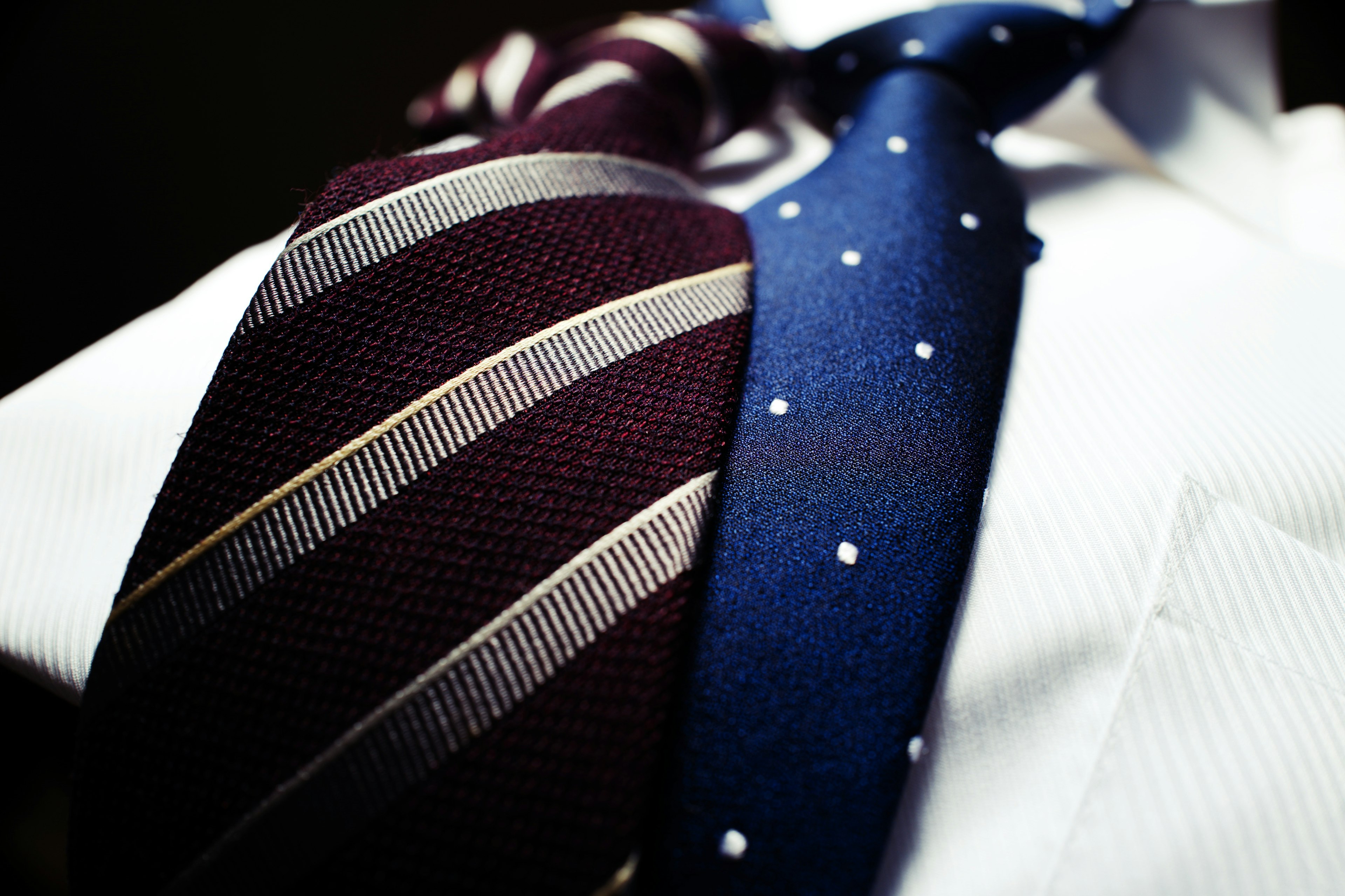 A close-up of a white shirt with a maroon striped tie and a blue polka dot tie