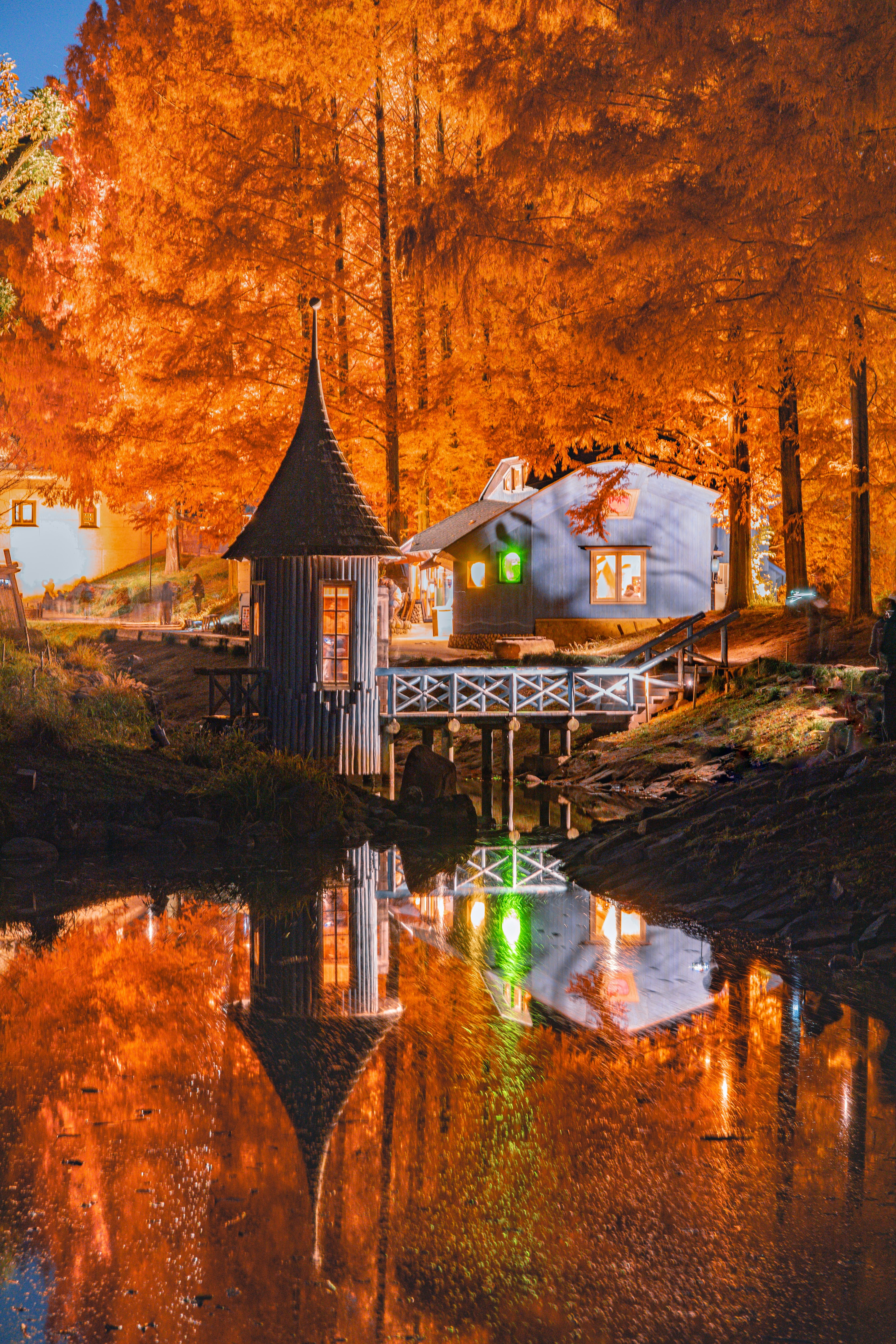 Ein kleines Haus umgeben von herbstlichen Farben, die sich in einem ruhigen See spiegeln