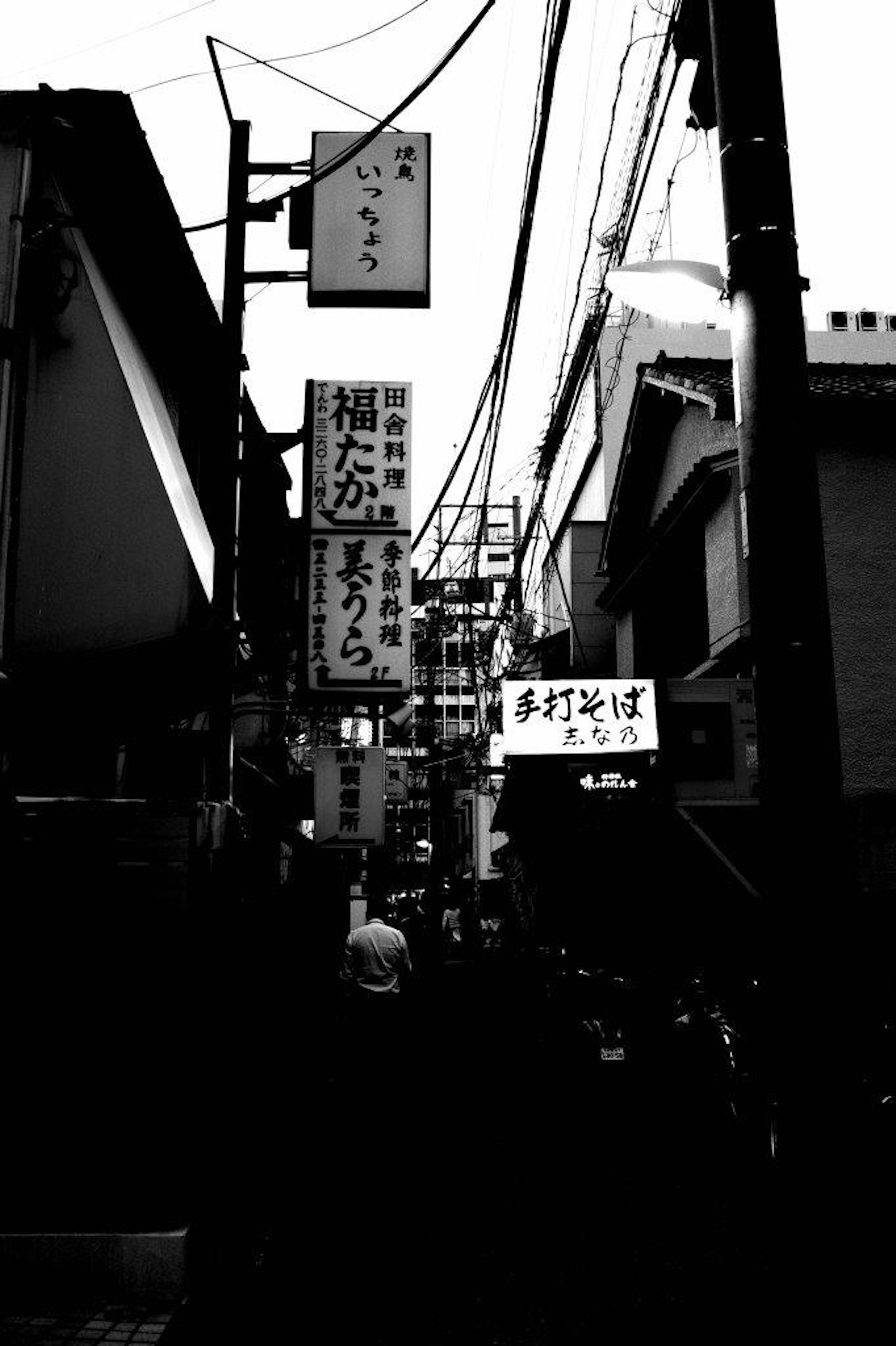 Calle estrecha con letreros y edificios en blanco y negro