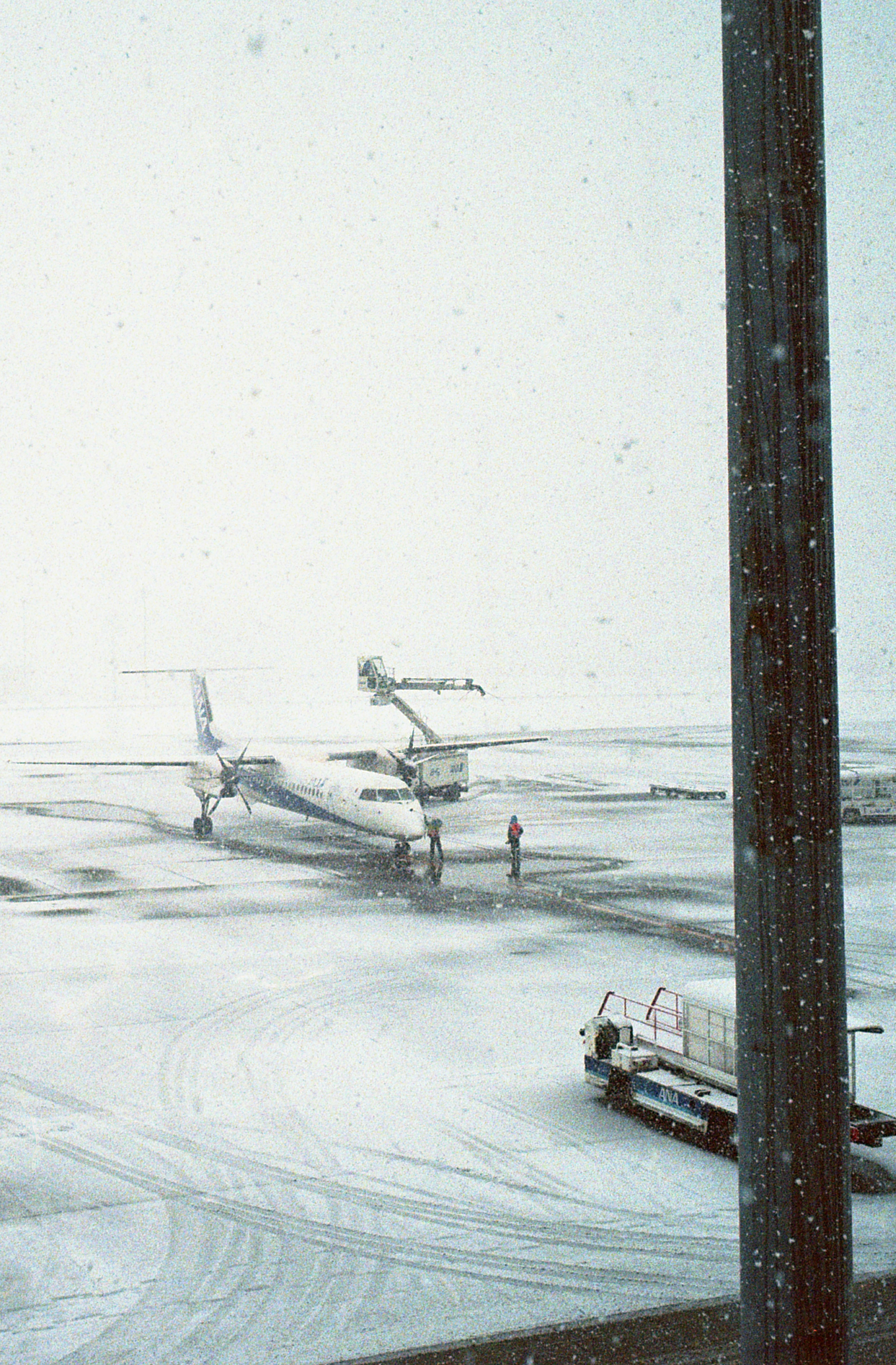 雪の中で滑走路に停まっている飛行機と作業員