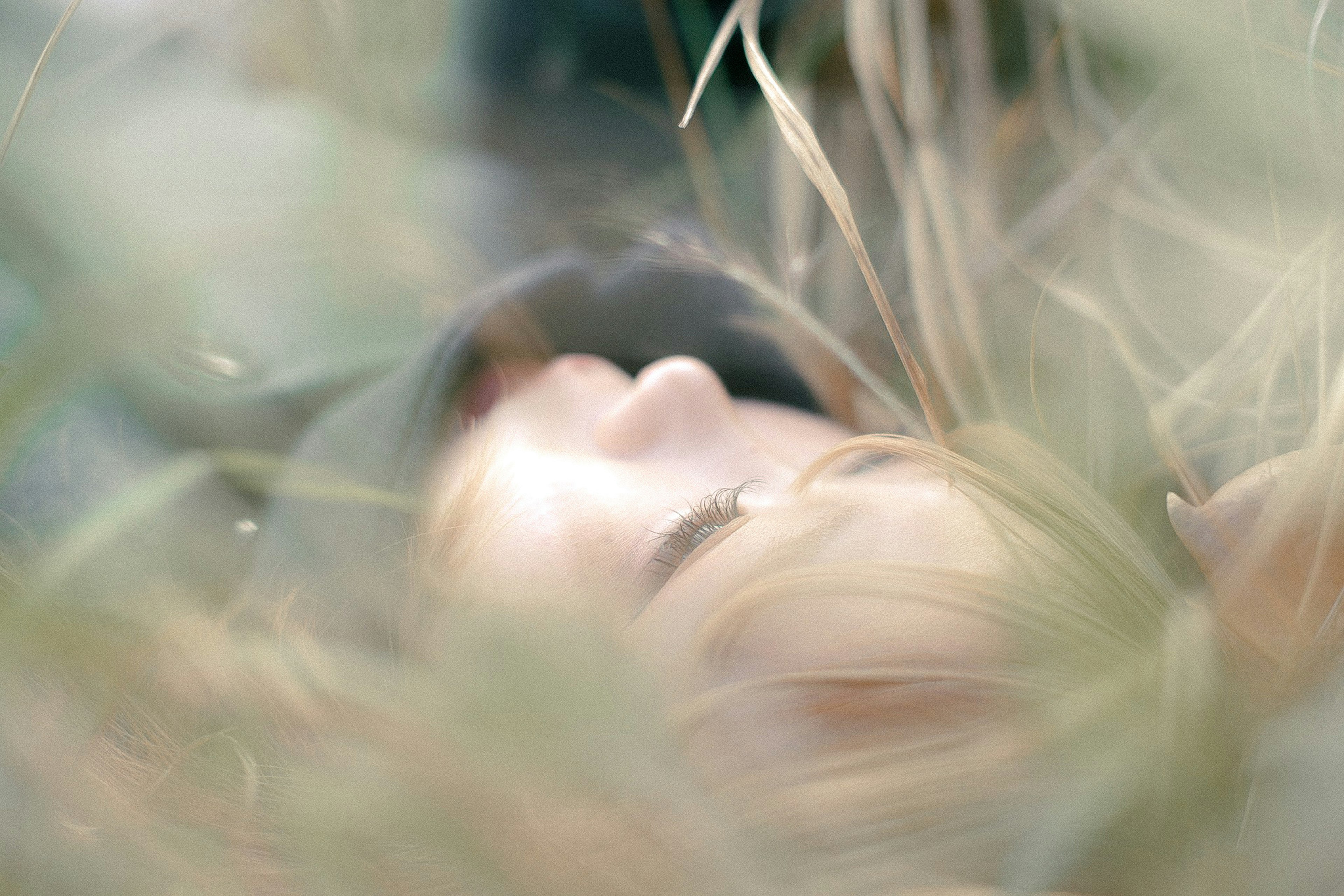 Close-up of a woman's face lying in grass soft color tones and blurred background