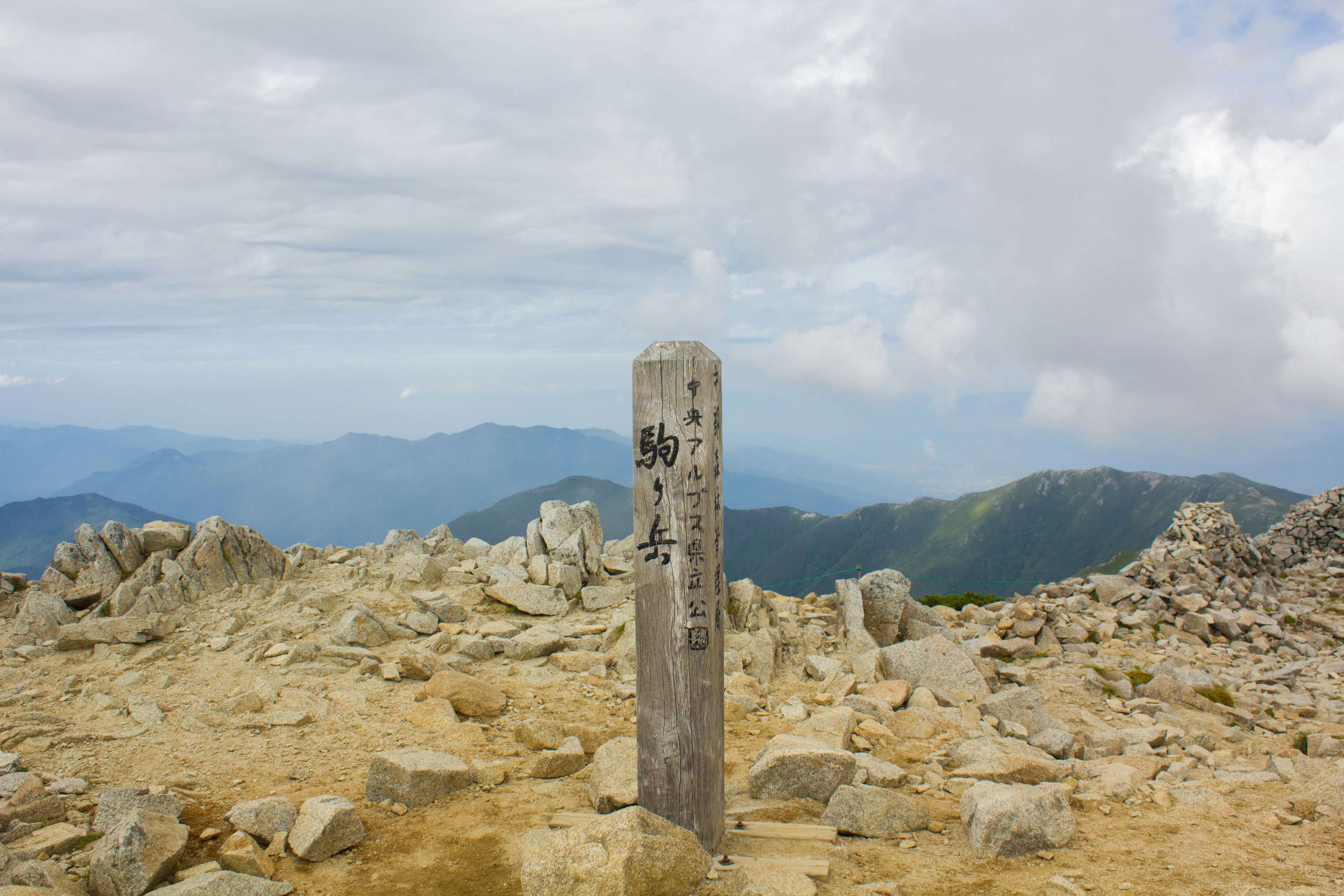 山の頂上に立つ標識と周囲の岩場の風景