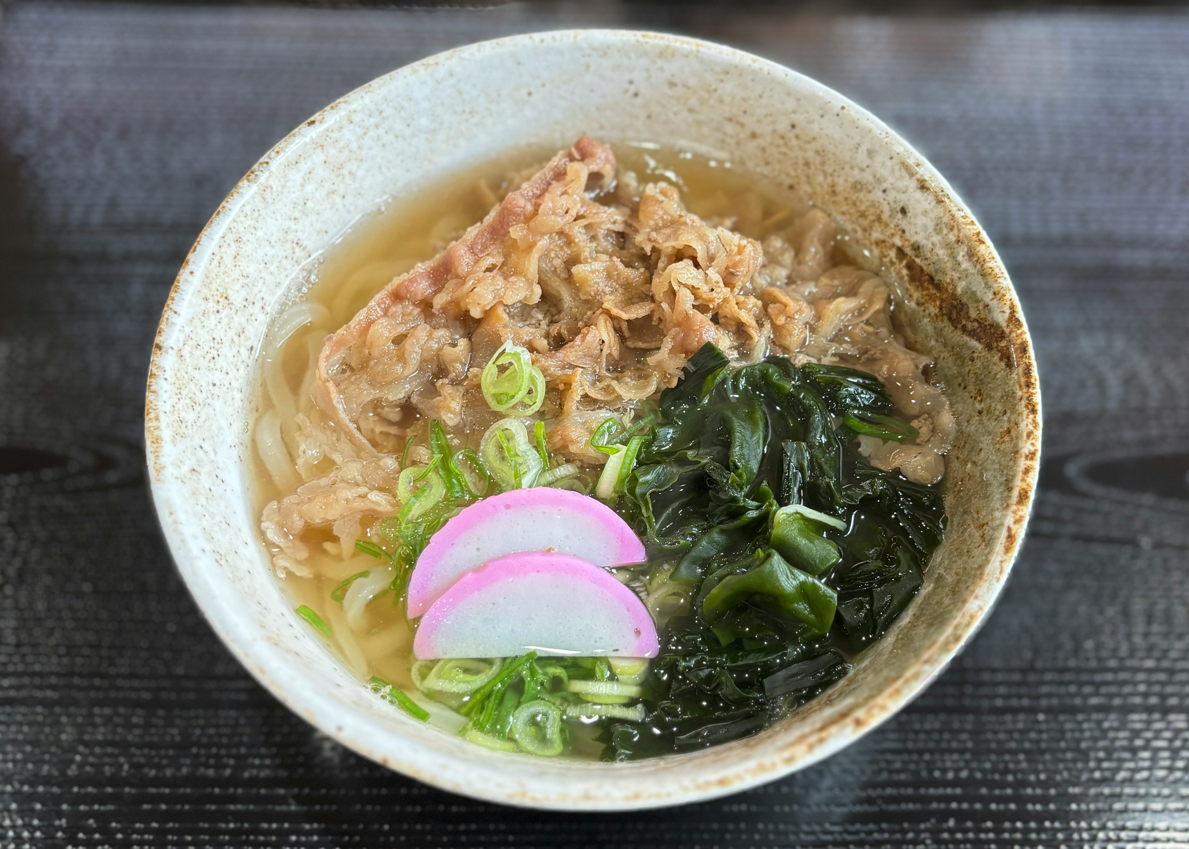 ラーメンのボウルには肉、ネギ、海藻、かまぼこが入っている