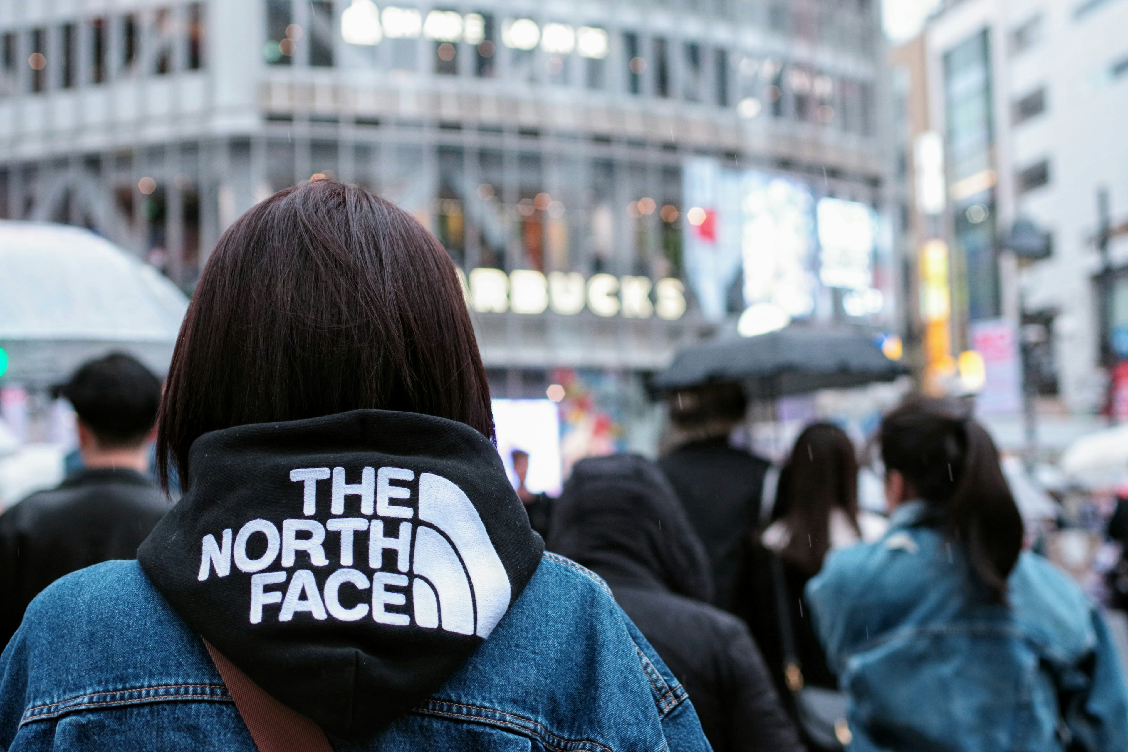 Wanita mengenakan hoodie THE NORTH FACE di jalanan kota yang ramai