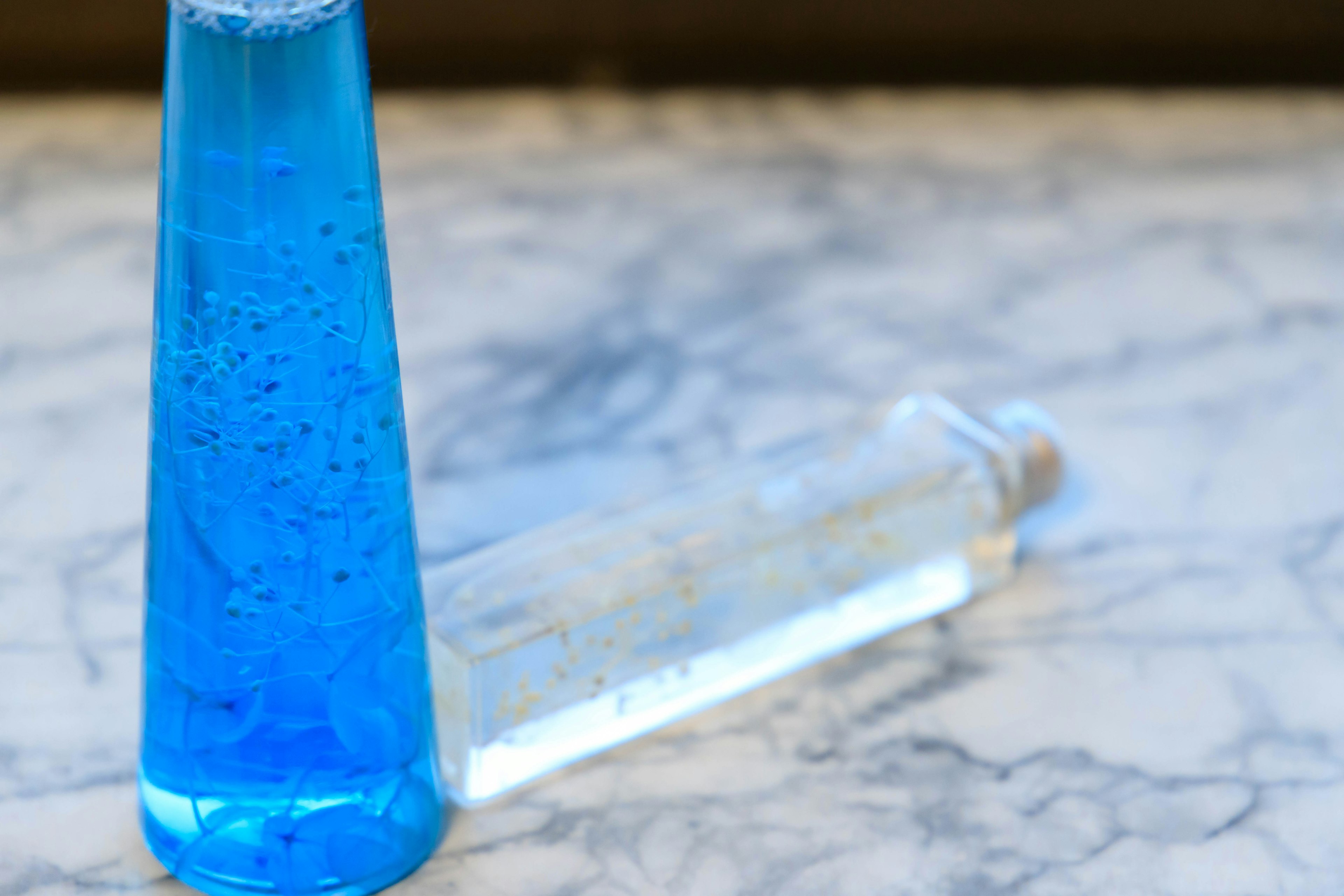 A blue liquid and a clear liquid in test tubes placed on a marble table