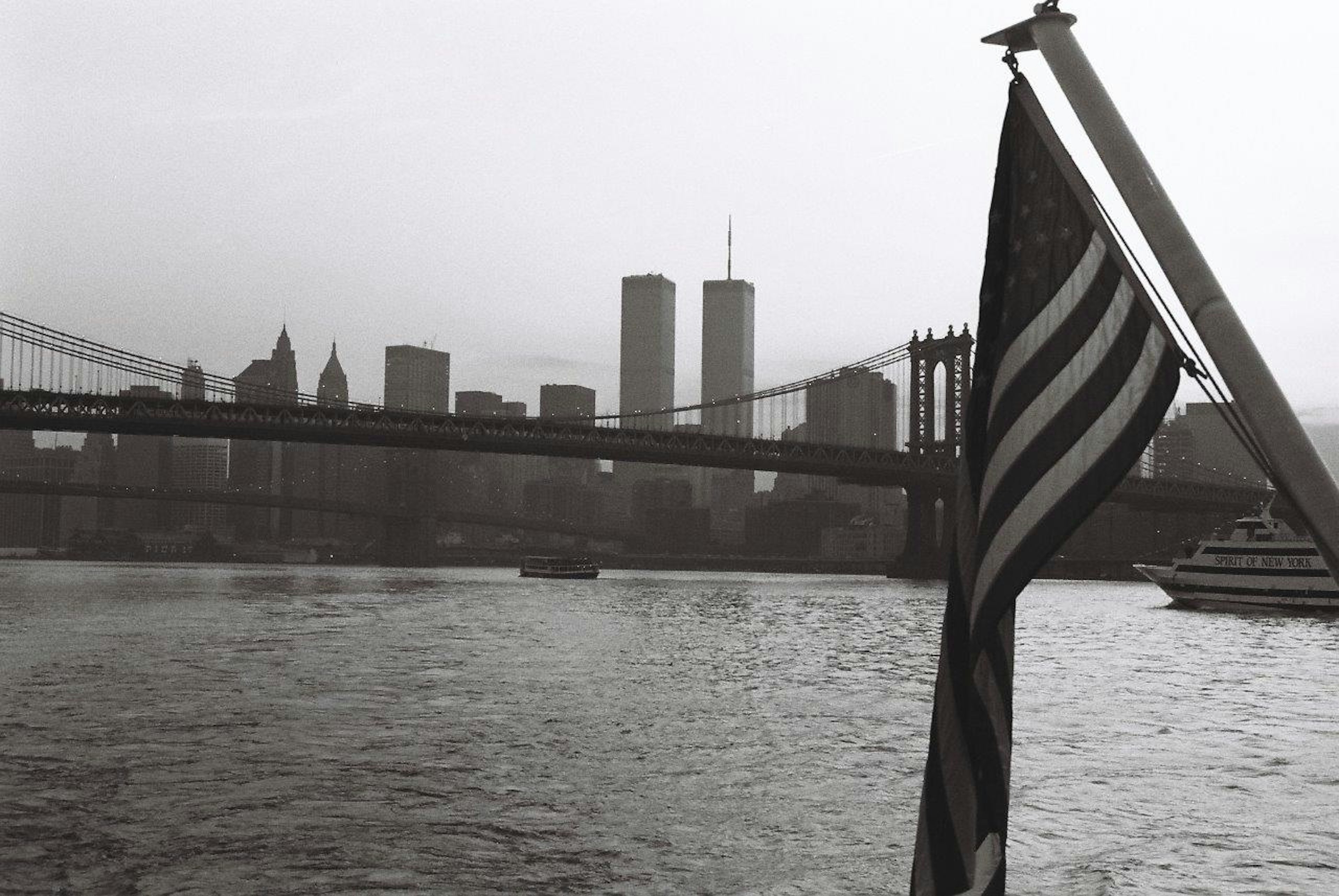 Black and white view of Manhattan skyline featuring the Twin Towers and an American flag in the foreground