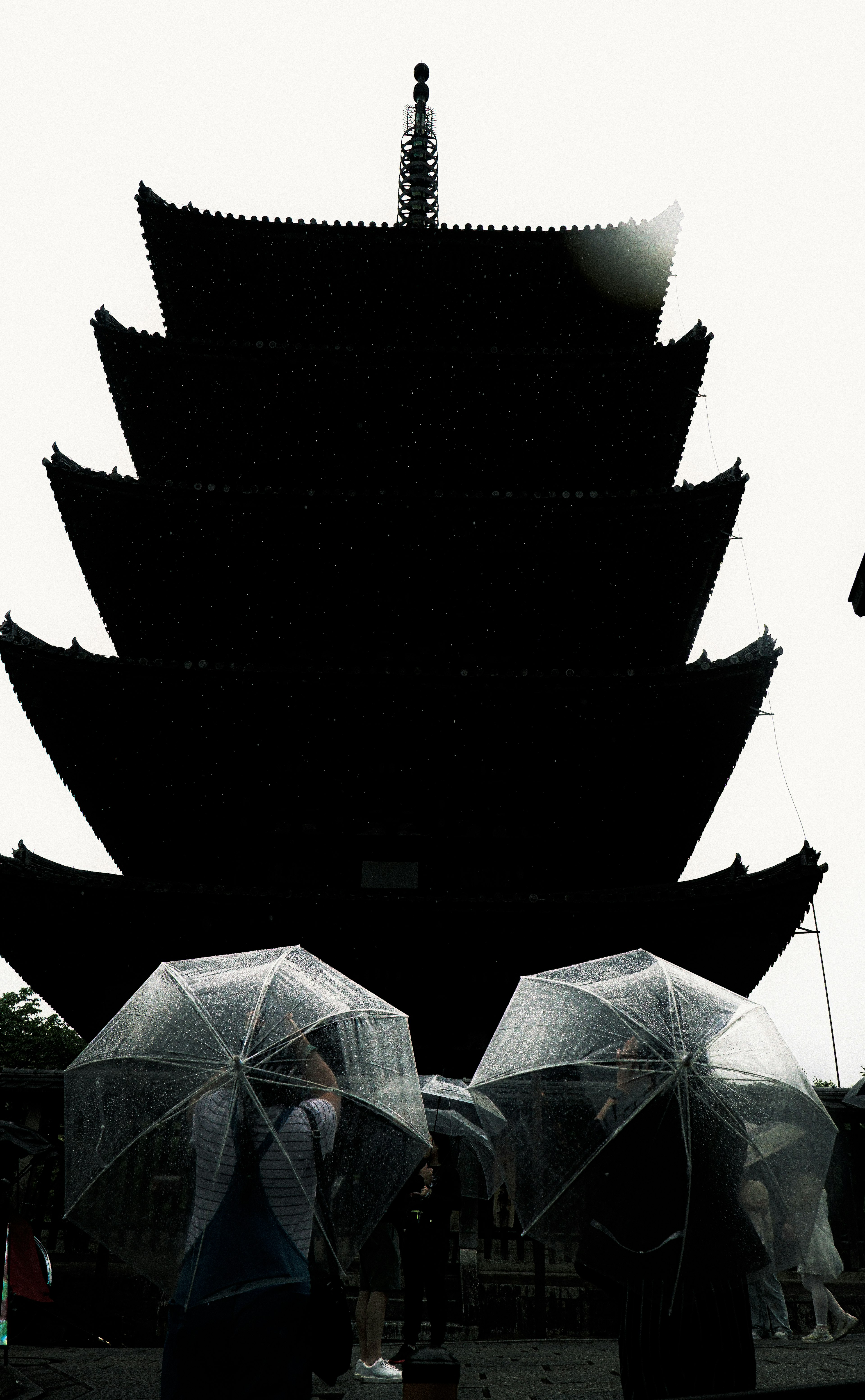 Silhouette of a pagoda with people holding transparent umbrellas on a rainy day