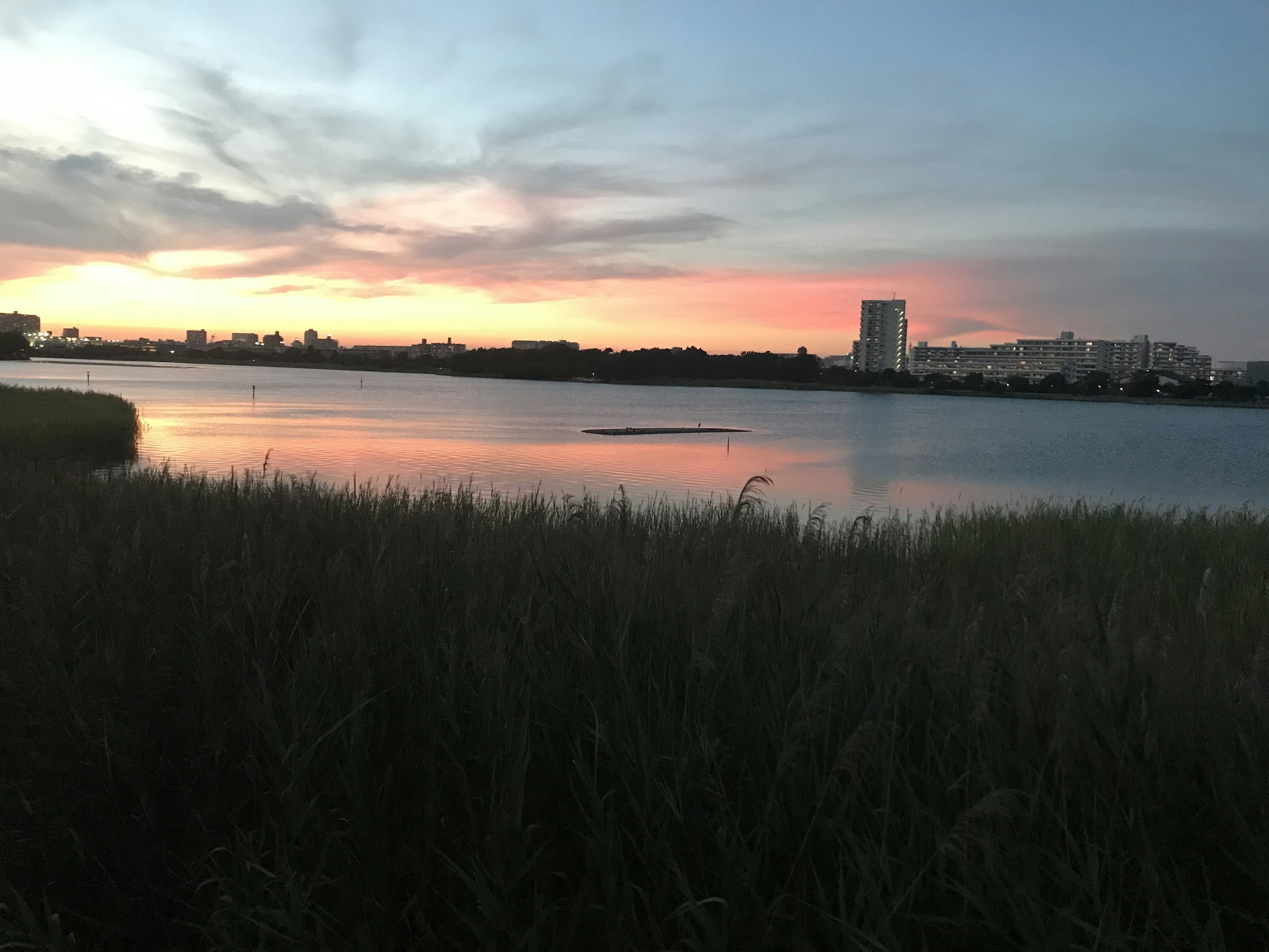 Paesaggio di un lago al tramonto con silhouette di alti edifici