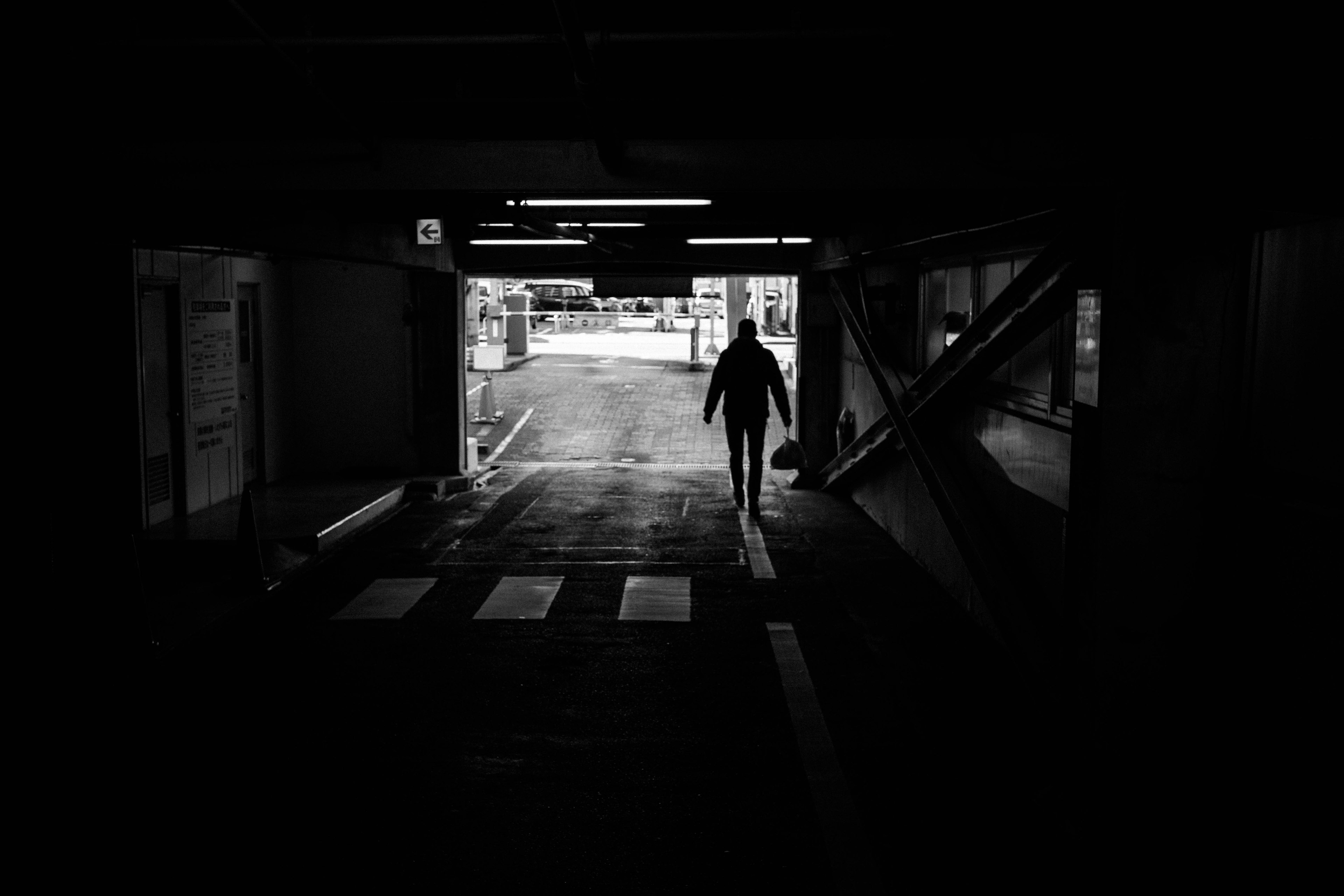 Silhouette di una persona che esce da un tunnel scuro con un attraversamento pedonale bianco