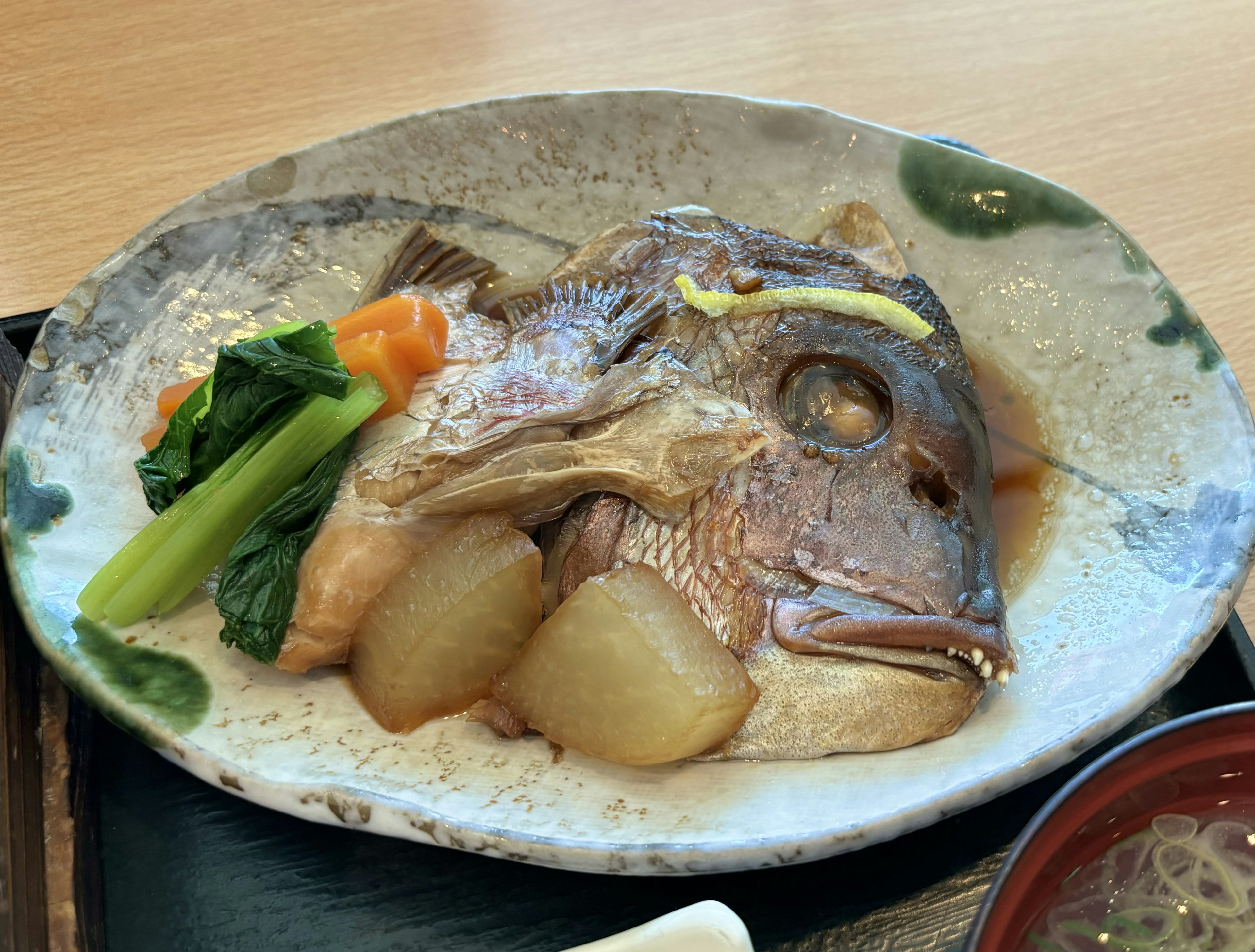 Ein wunderschön angerichtetes Fischgericht auf einem Keramikteller mit einem ganzen Fisch, garniert mit Daikon und grünen Gemüse