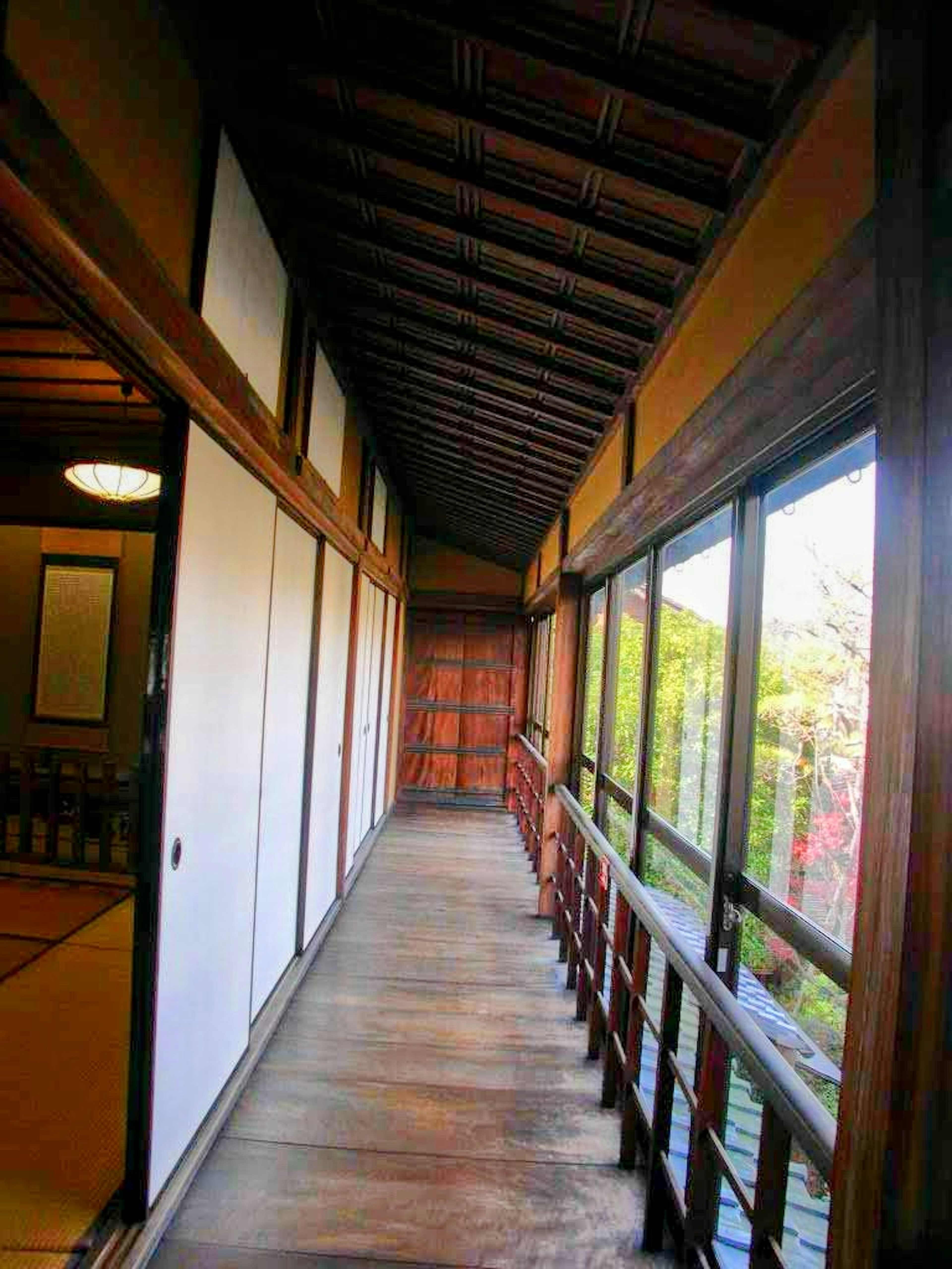 Couloir d'une maison japonaise traditionnelle avec des sols et murs en bois donnant sur la verdure à travers de grandes fenêtres