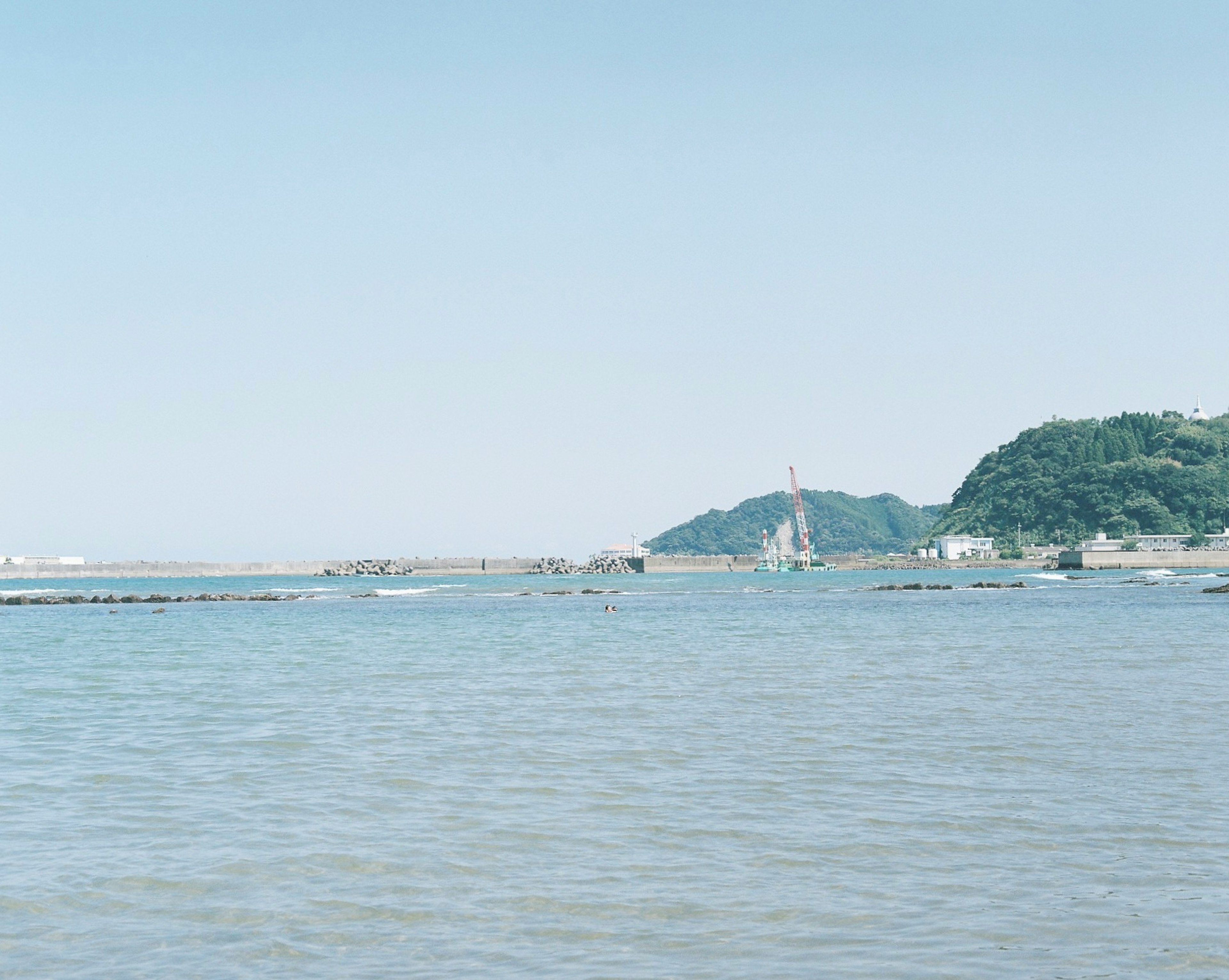 青い海と穏やかな波の景色、遠くの山と建物が見える