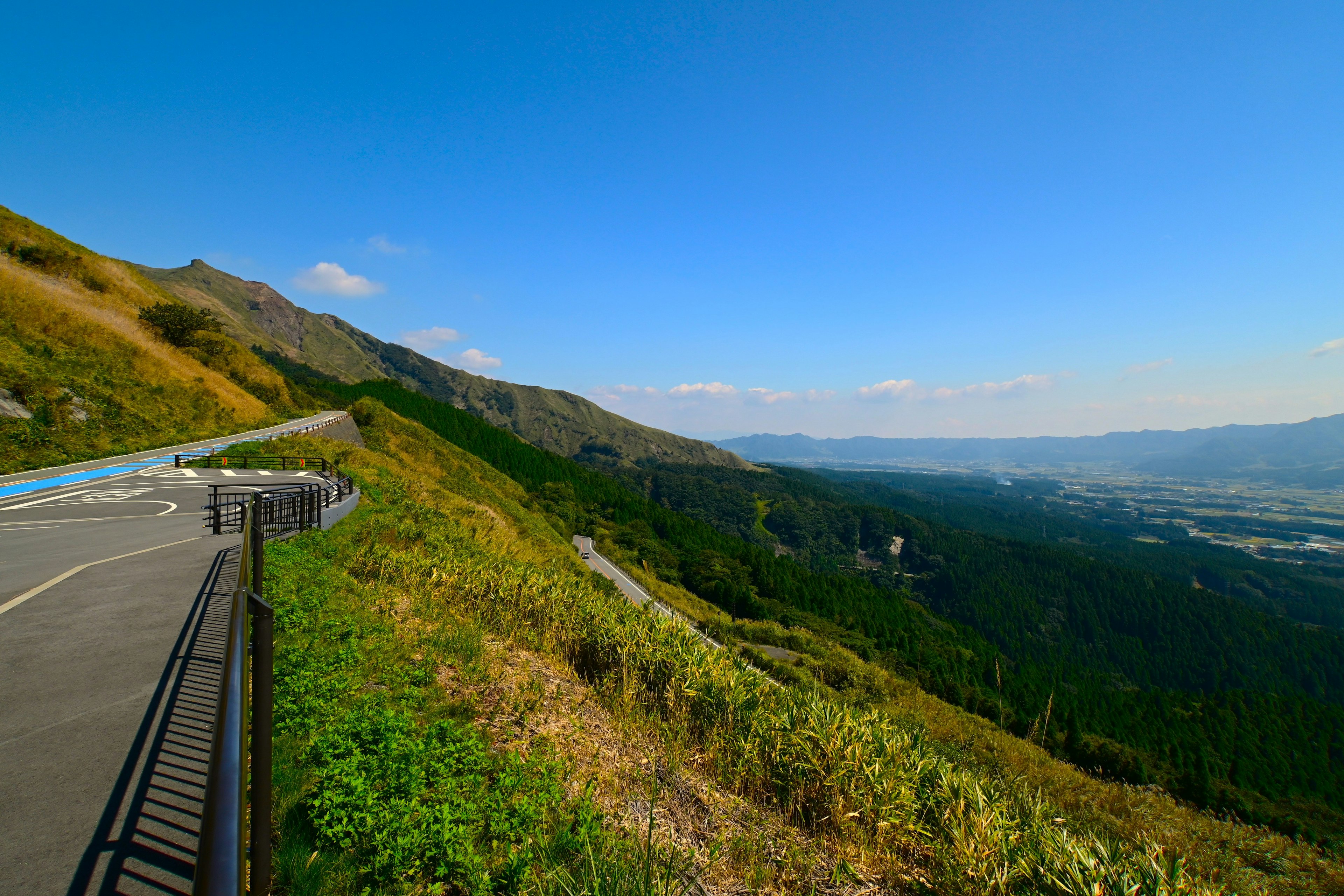 Malersicher Blick auf eine kurvenreiche Straße entlang eines Berghangs mit üppigem Grün und klarem blauen Himmel