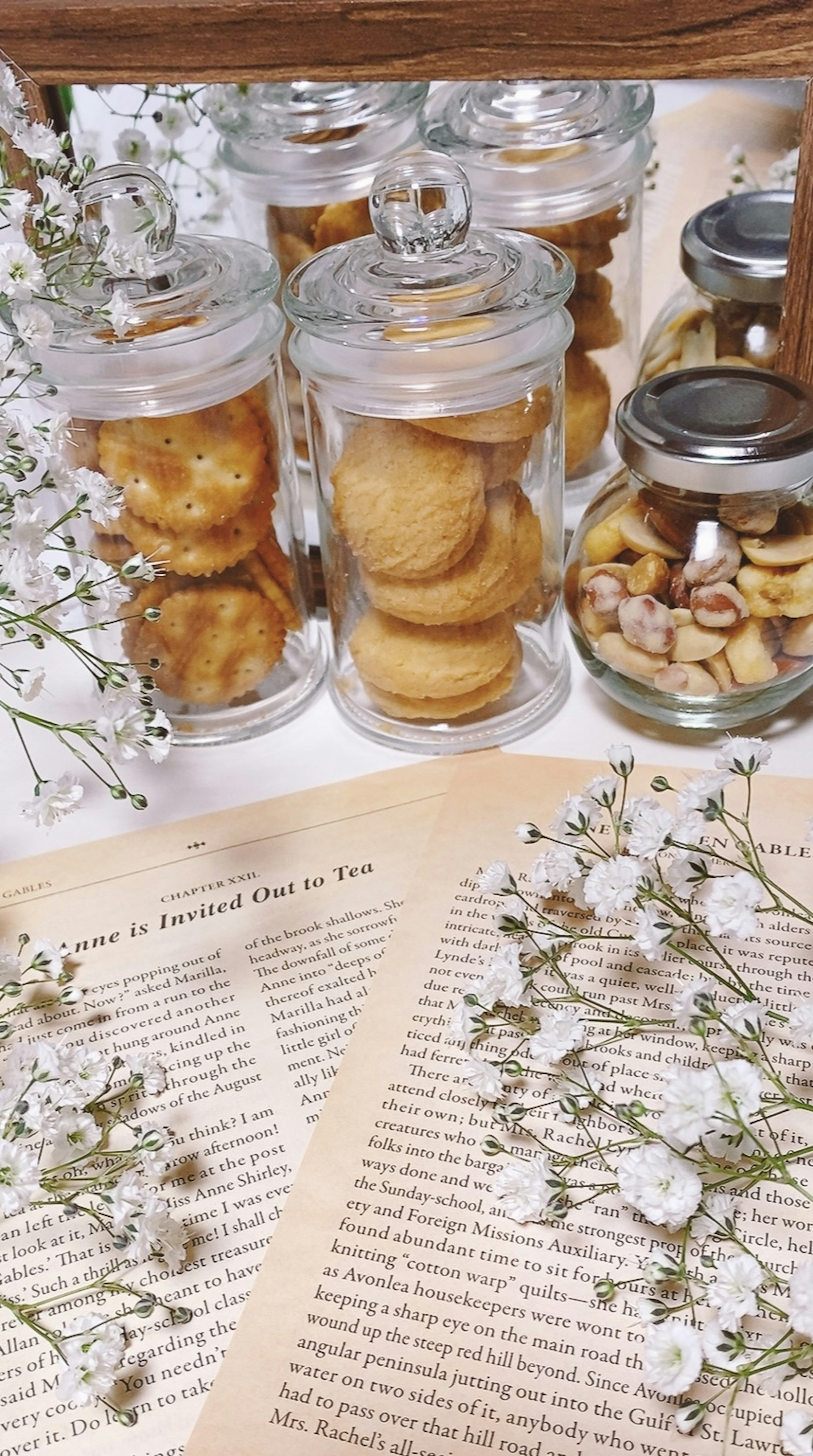 Una mesa con un libro abierto rodeado de tarros de vidrio llenos de galletas y decorado con flores