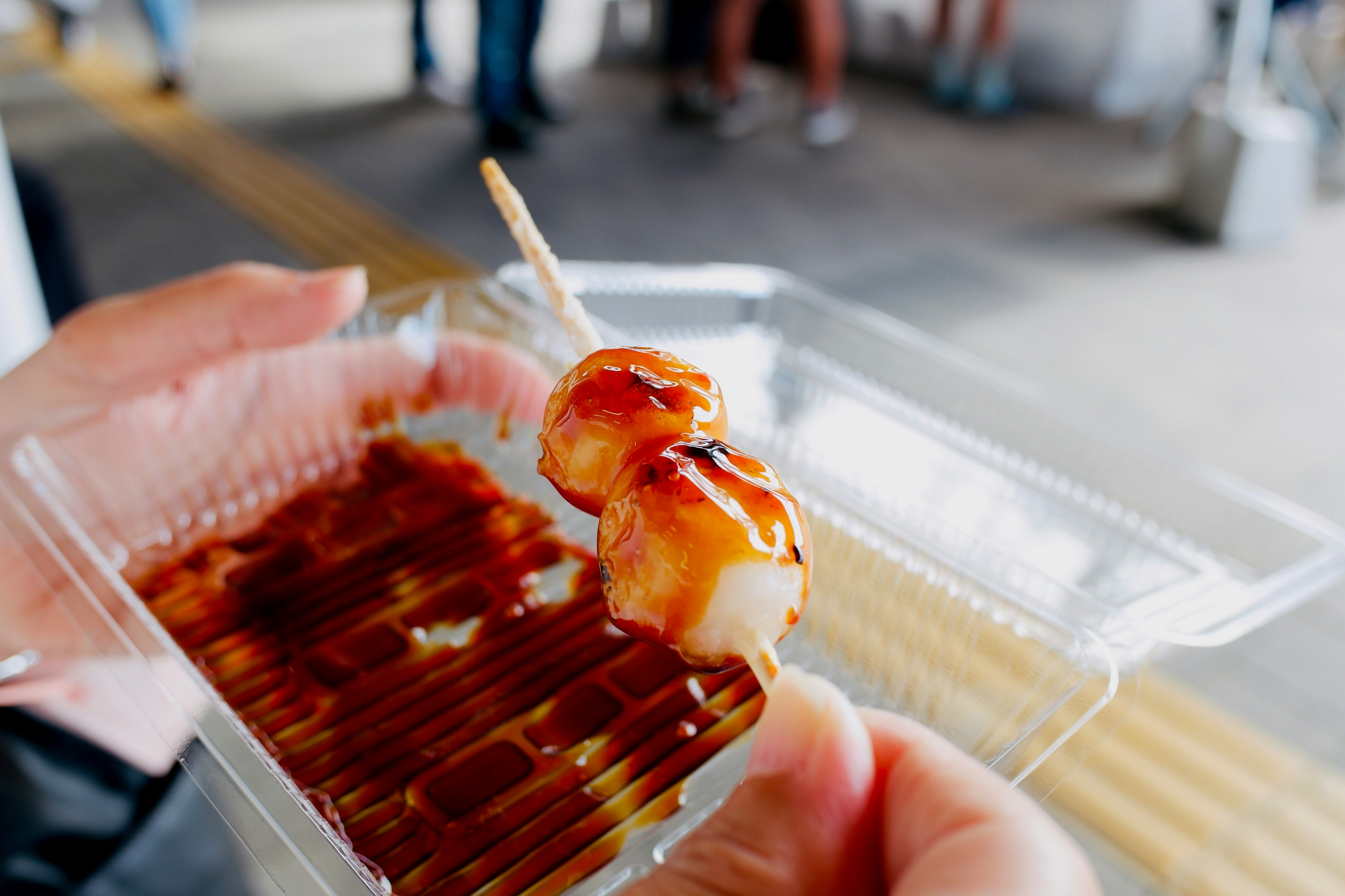 手に持たれた串焼きの食べ物と甘いタレがかかった様子