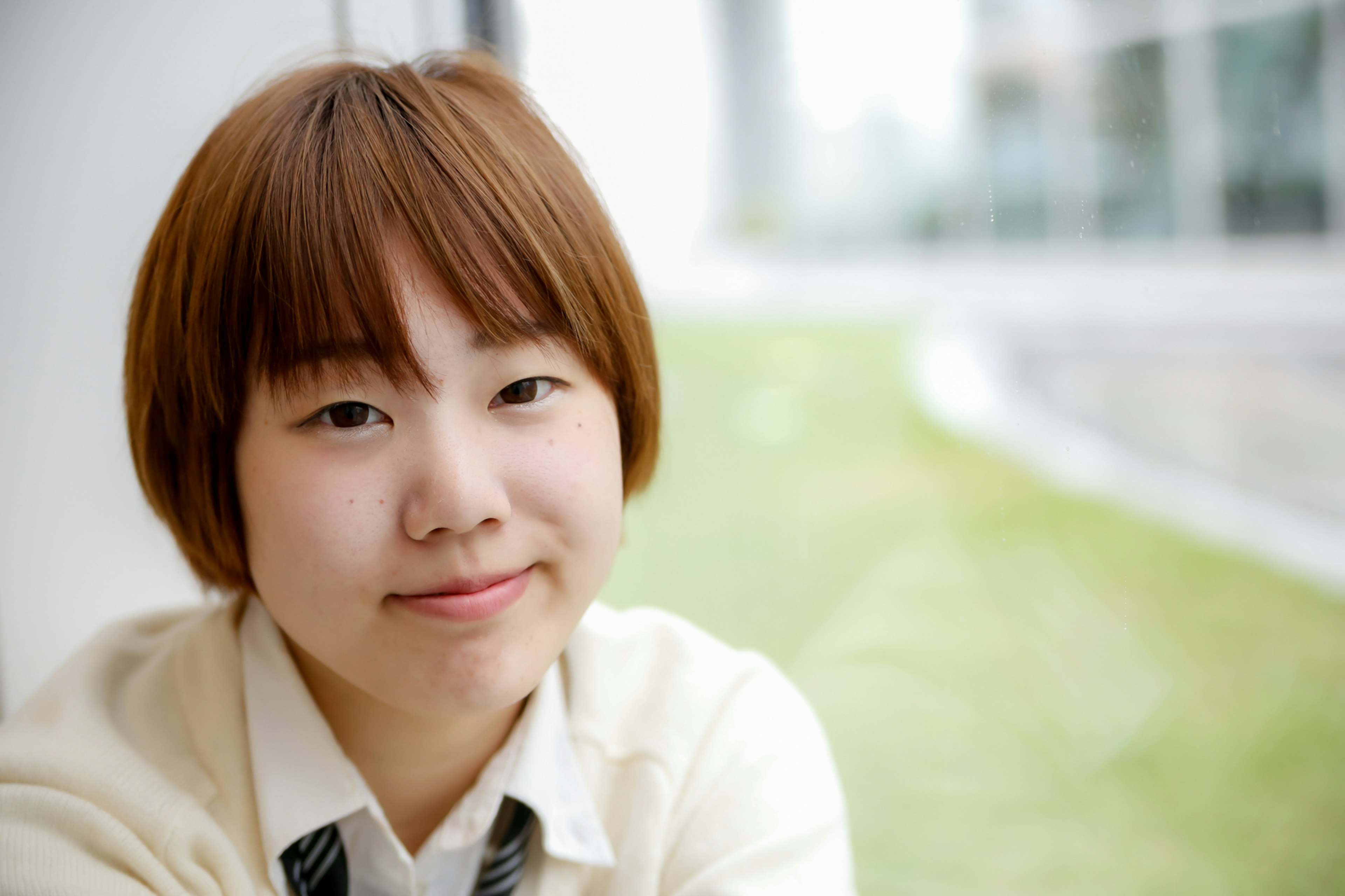 Portrait of a young woman smiling with green grass and bright window in the background