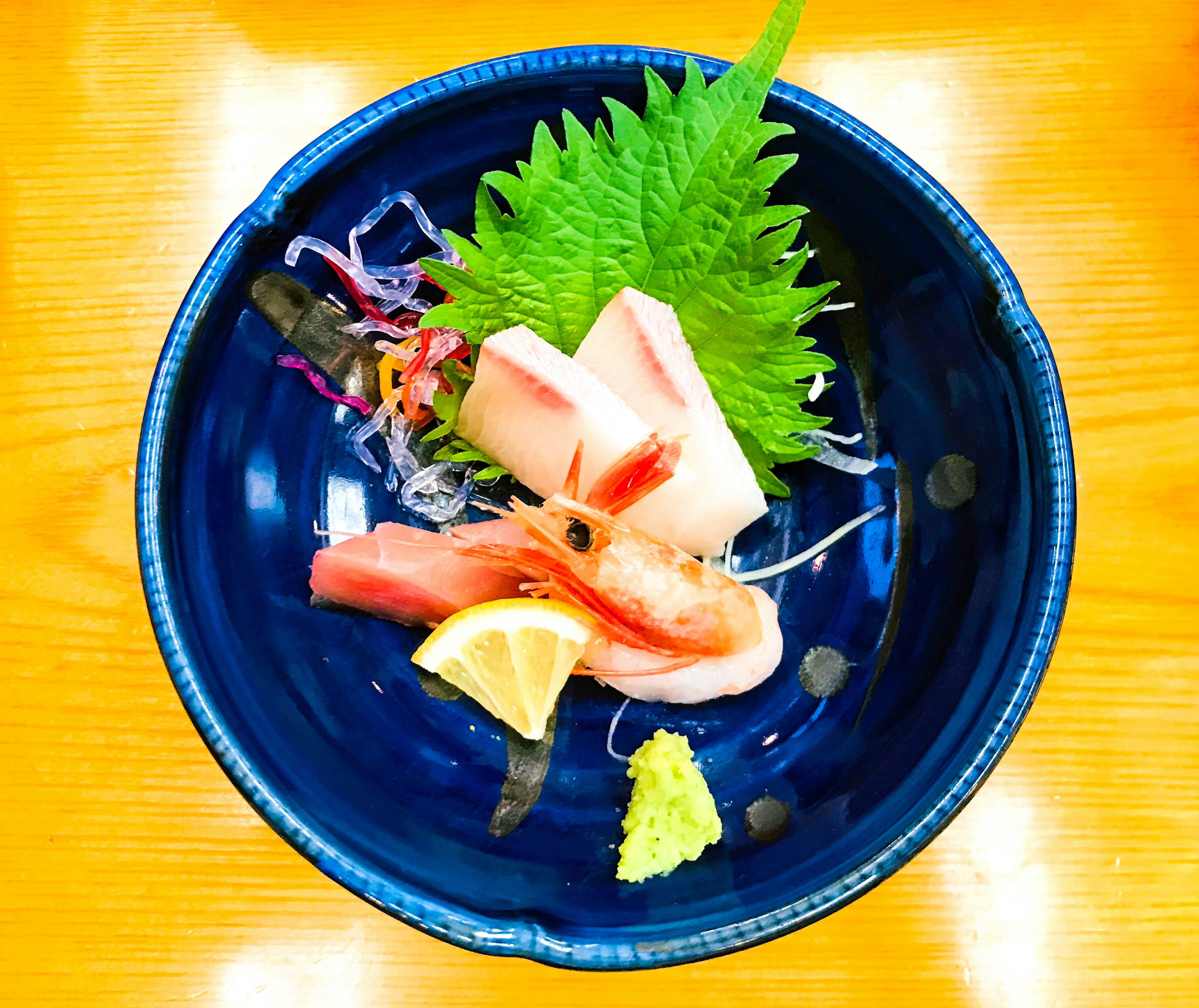 Sashimi frais servi dans une assiette bleue avec des feuilles de shiso et des garnitures