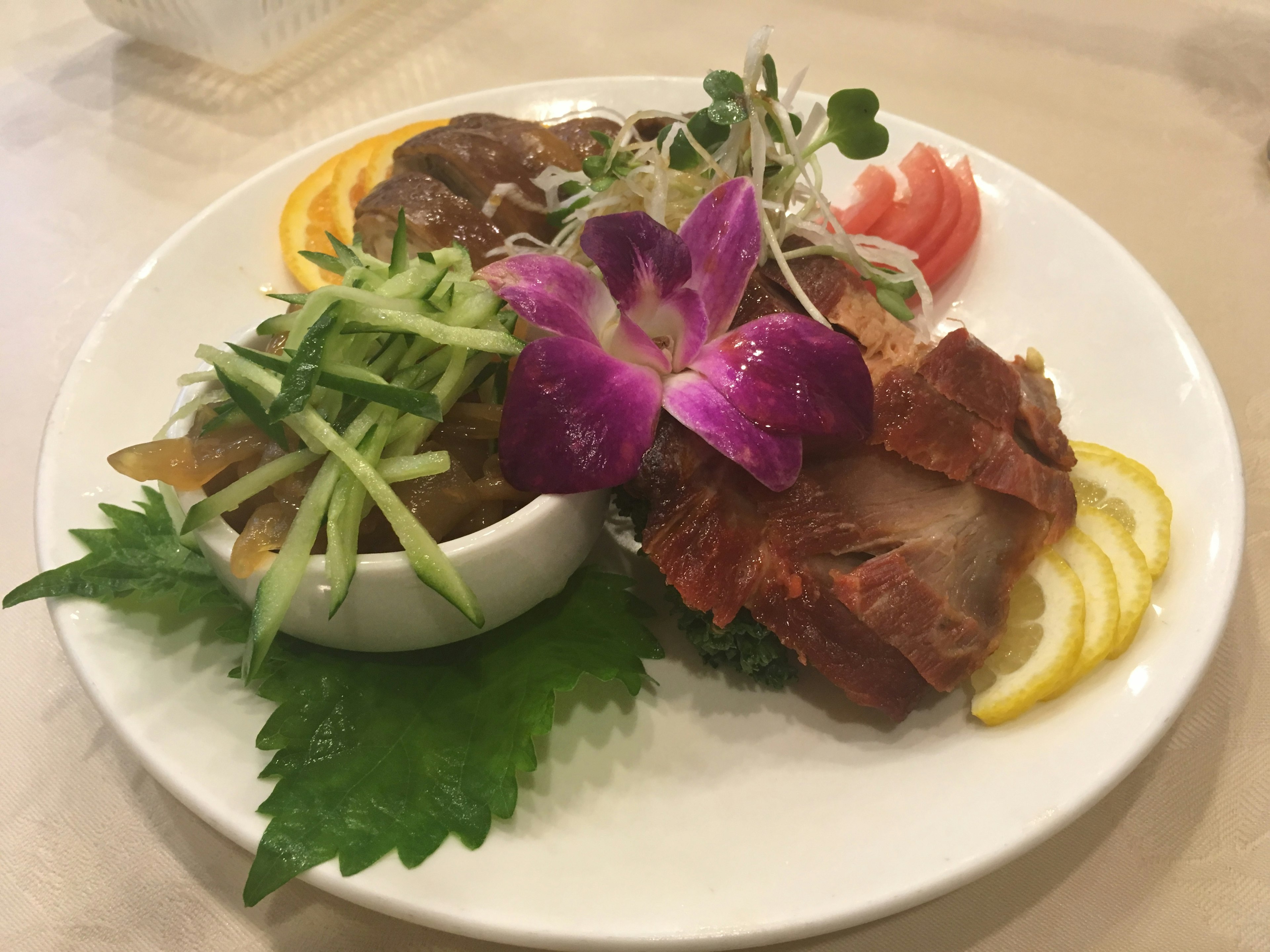 Elegant dish presentation with sliced fish and meat garnished with fresh vegetables and flowers