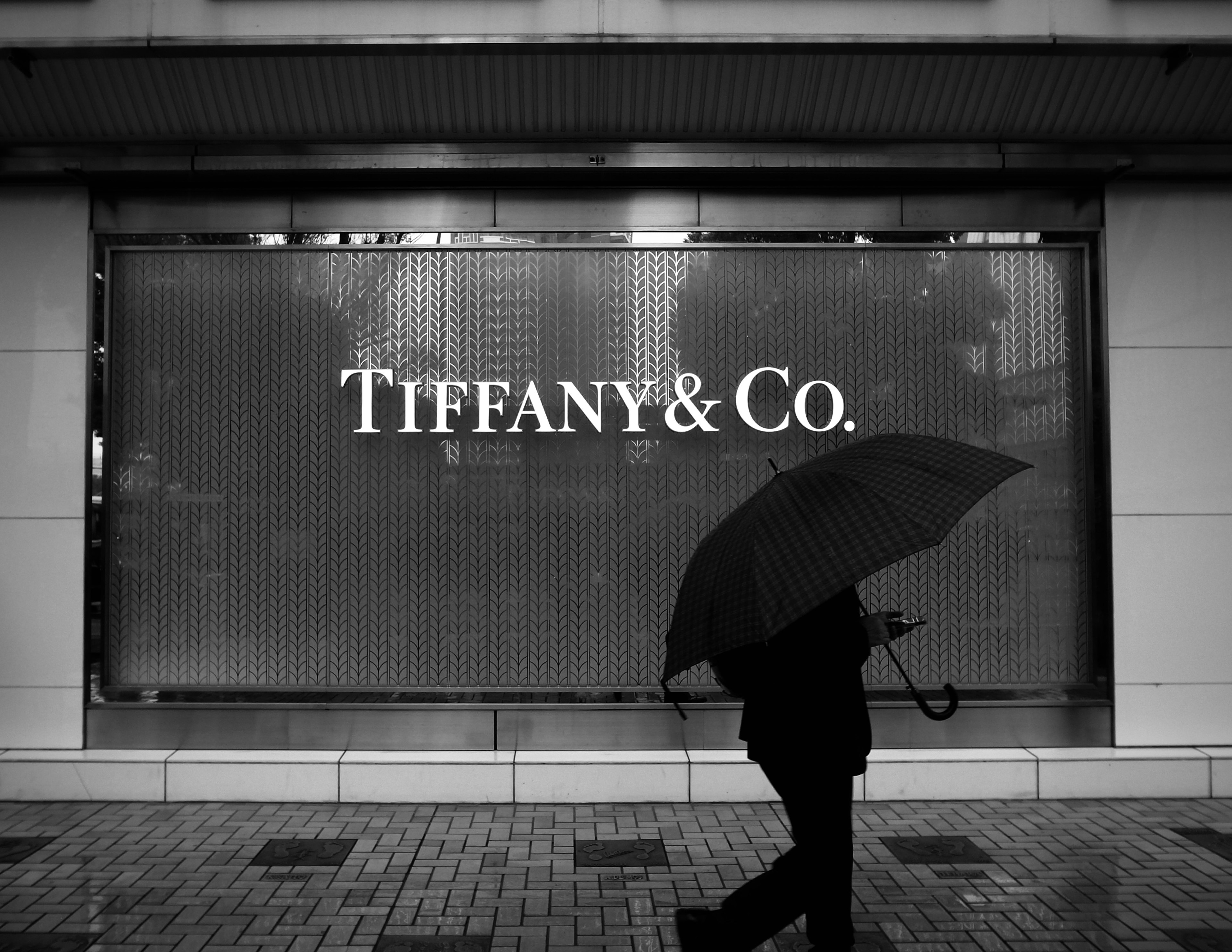 Silhouette of a person walking with an umbrella in front of a Tiffany & Co. store