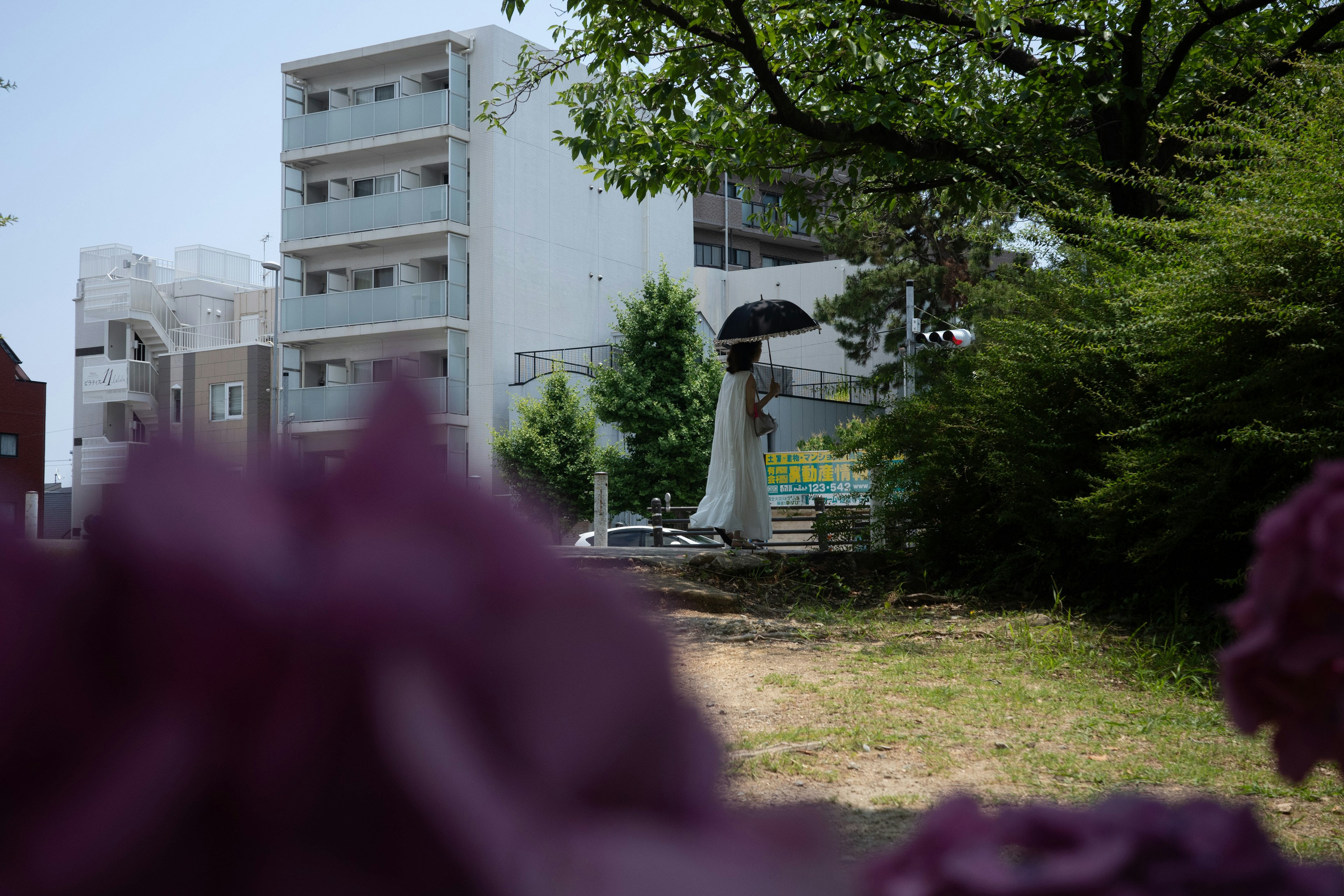 一座女性手持雨傘的雕像位於白色建築和綠樹前面