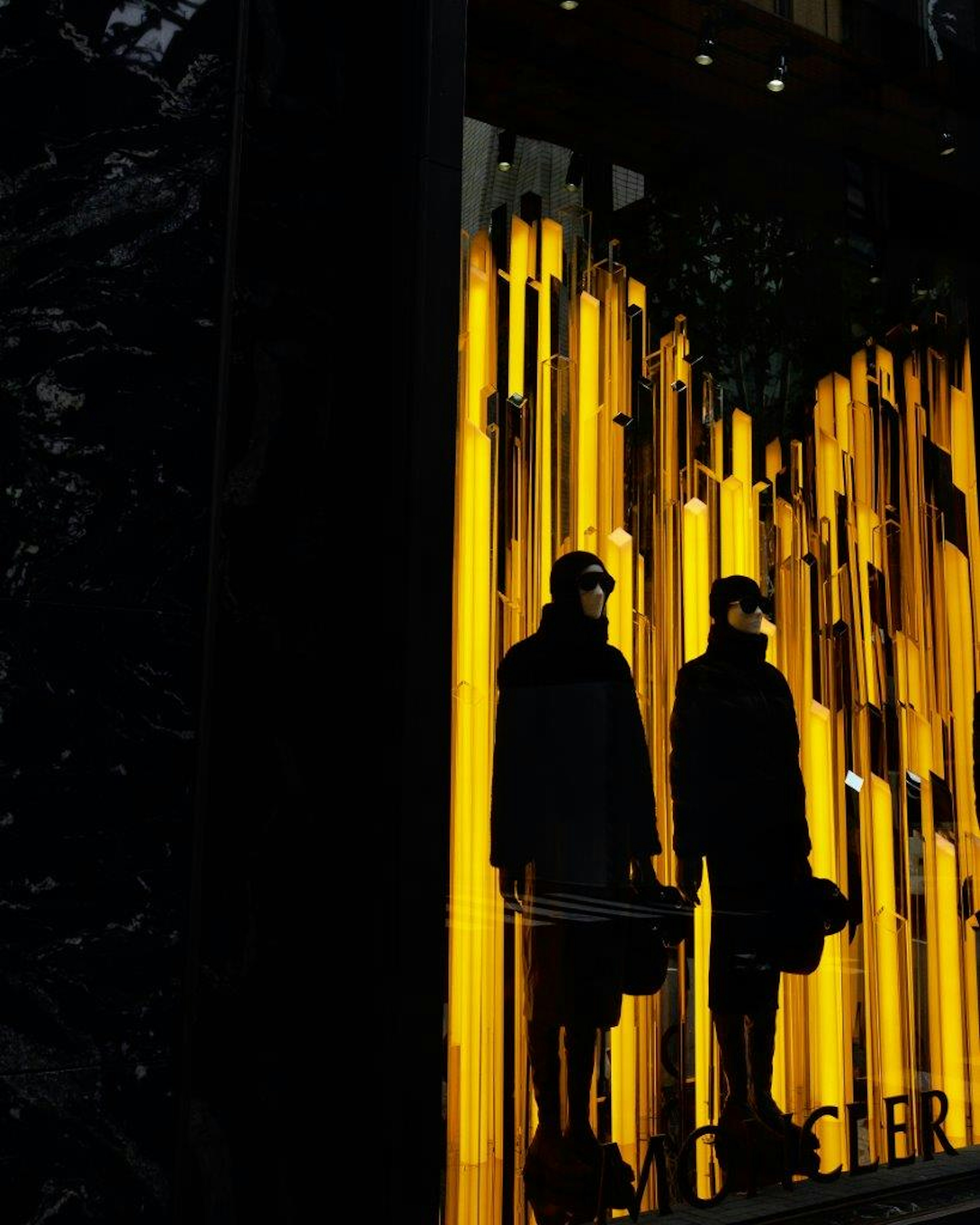 Dos figuras en abrigos negros reflejadas contra un fondo de luces amarillas