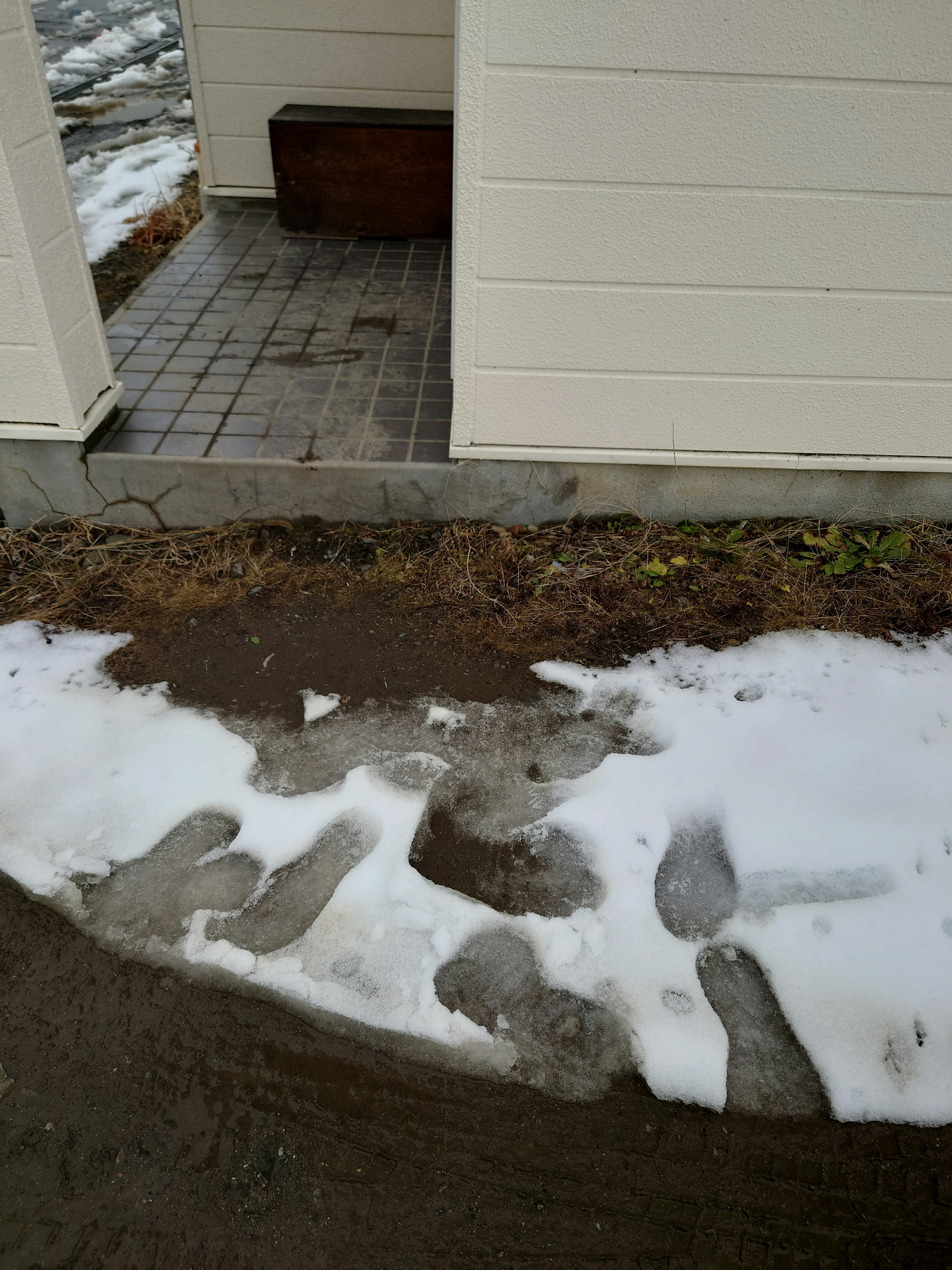 Footprints in snow alongside a dirt path and tiled entrance