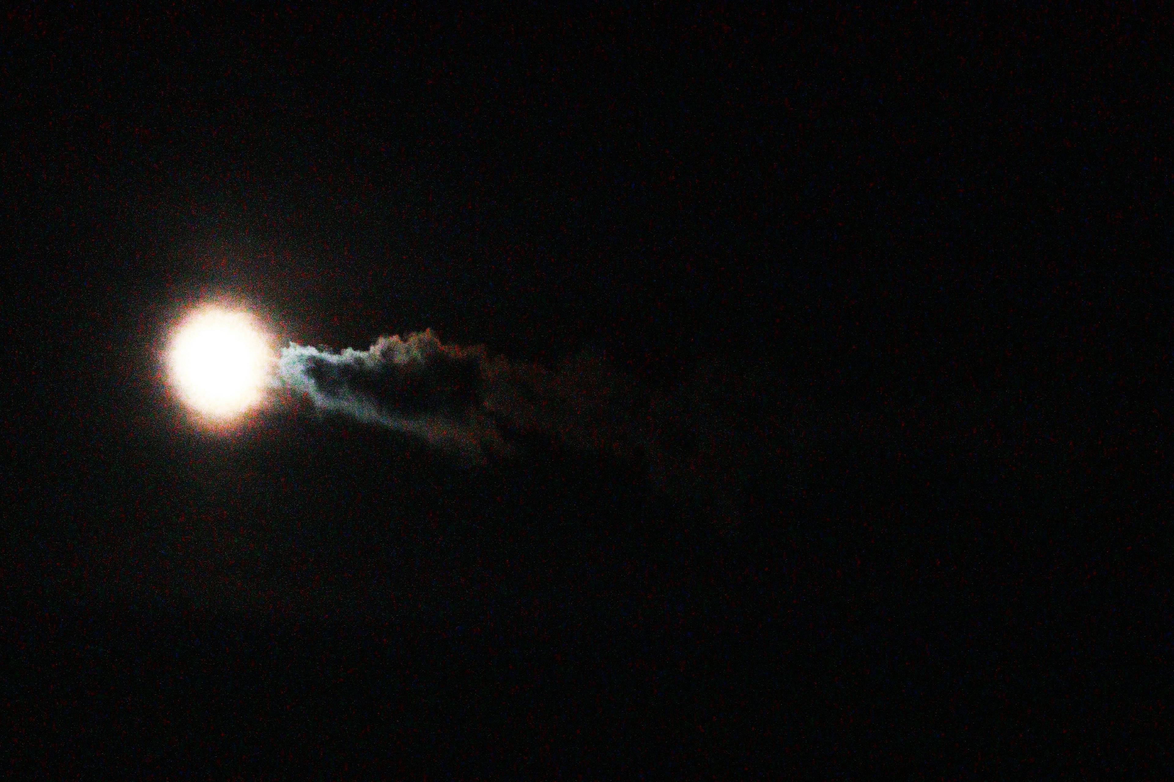 Bright moon in the night sky with wisps of smoke trailing