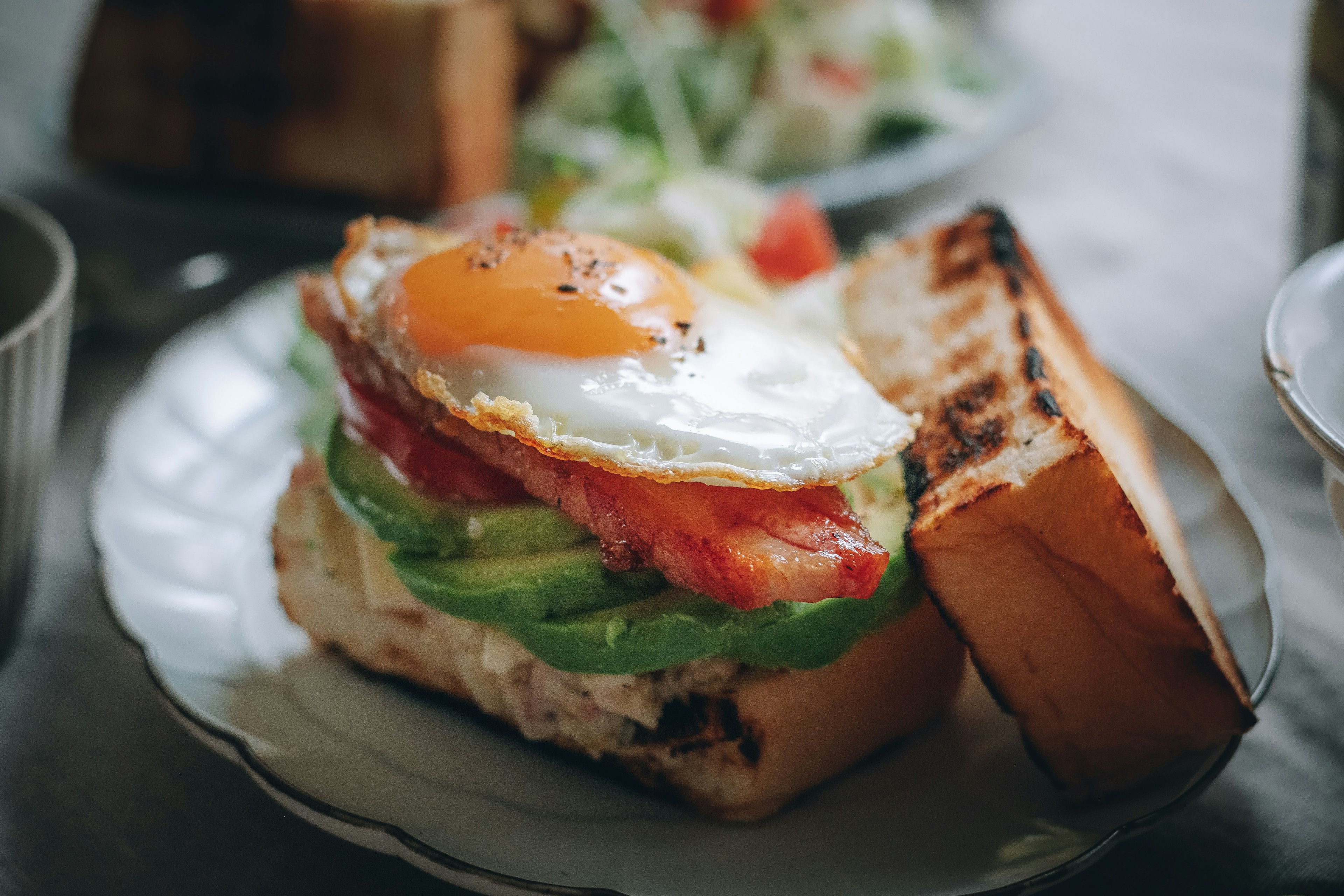 Un sándwich con tostada, lechuga, tocino y un huevo frito