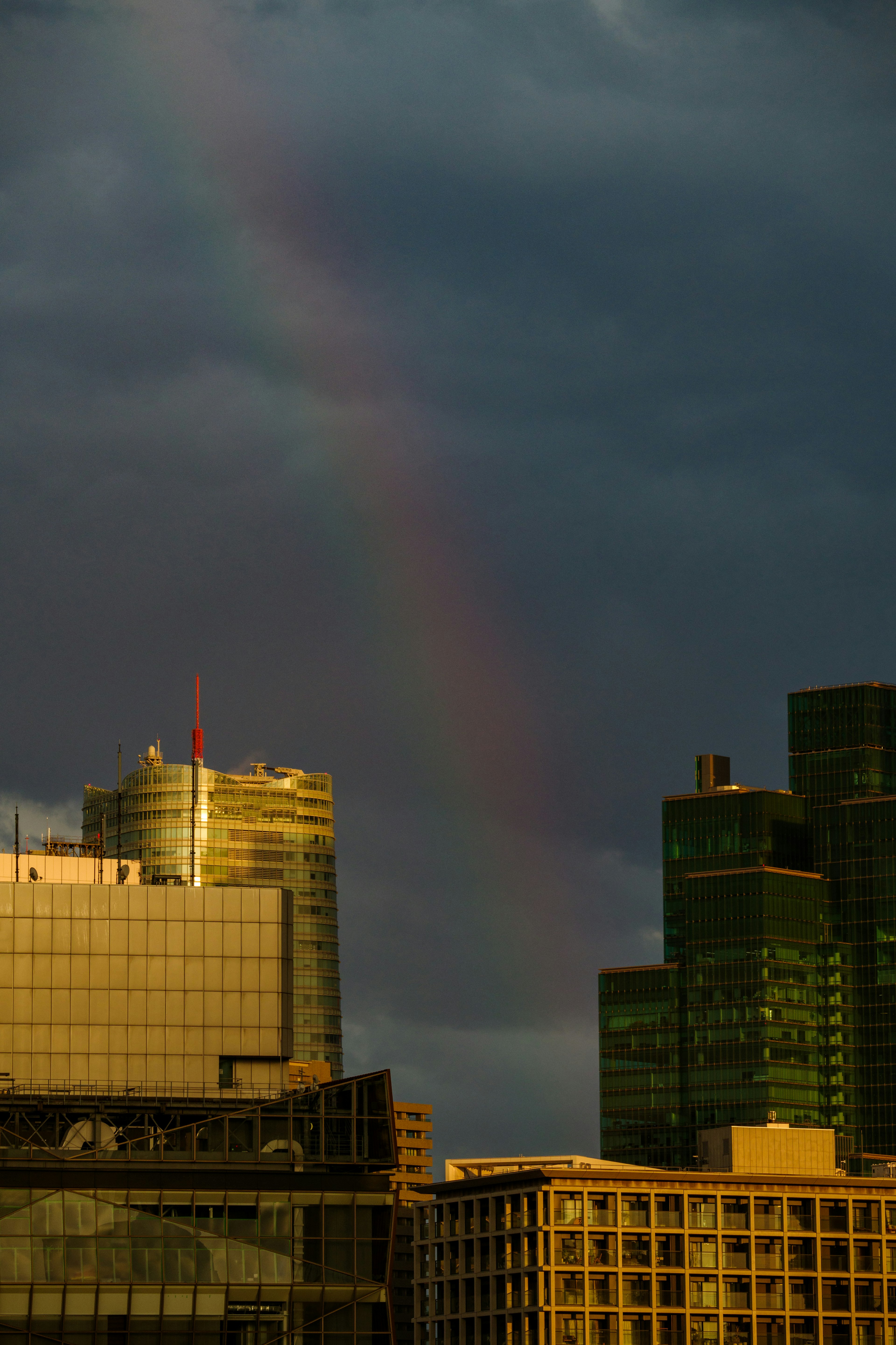 Rainbow appearing through dark clouds above city skyline