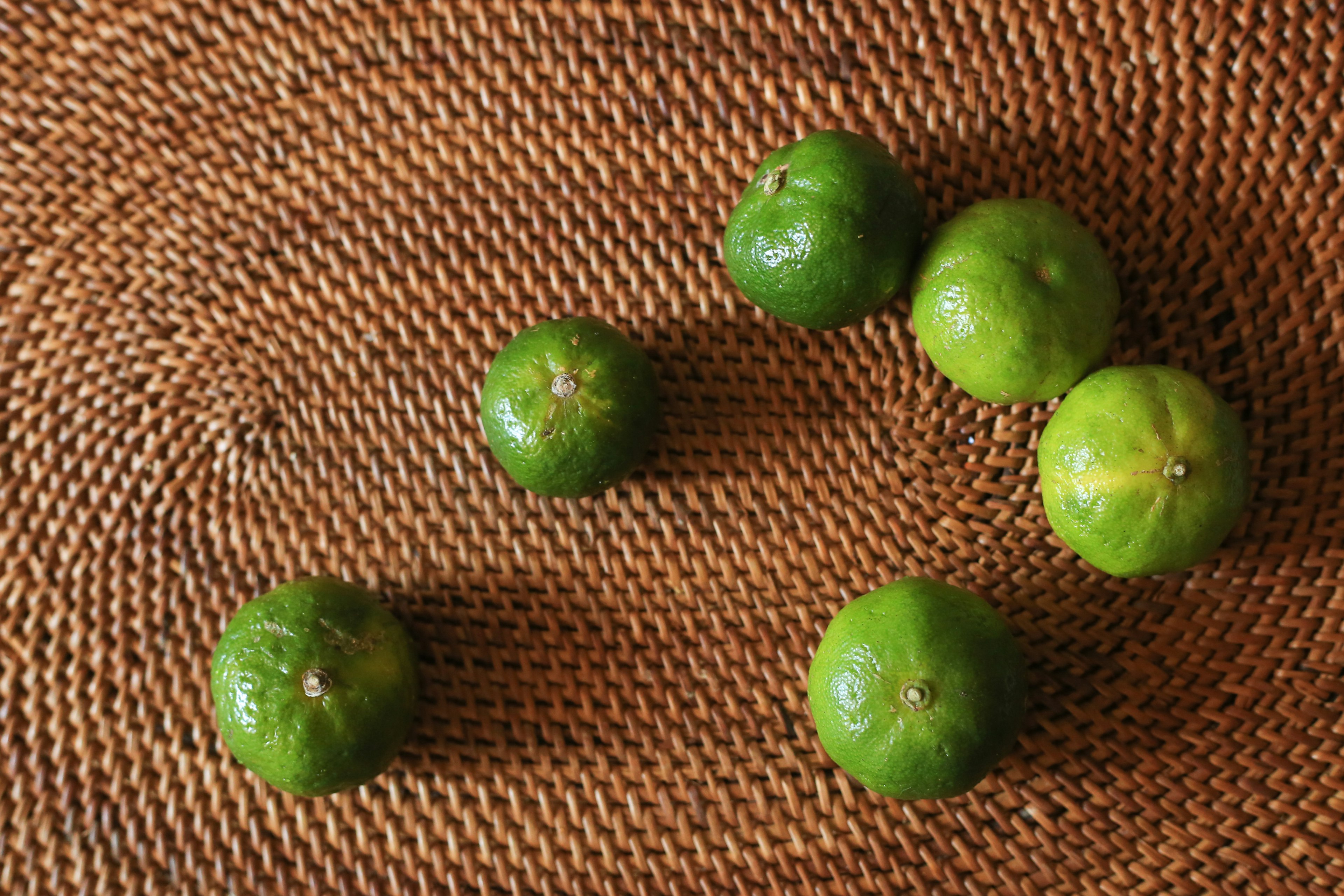 Green citrus fruits arranged on a woven brown background