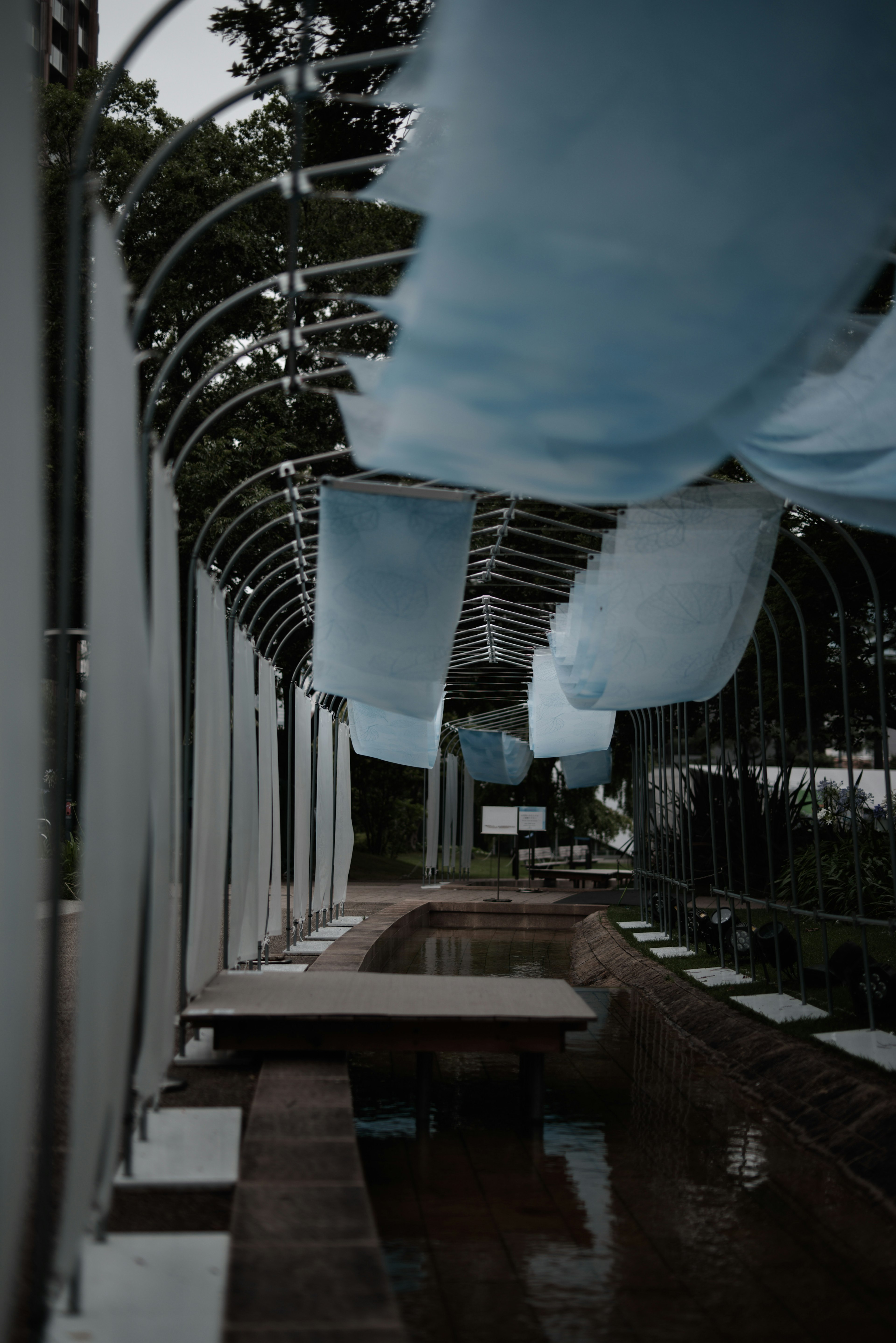 An outdoor structure with flowing blue fabric and wooden benches