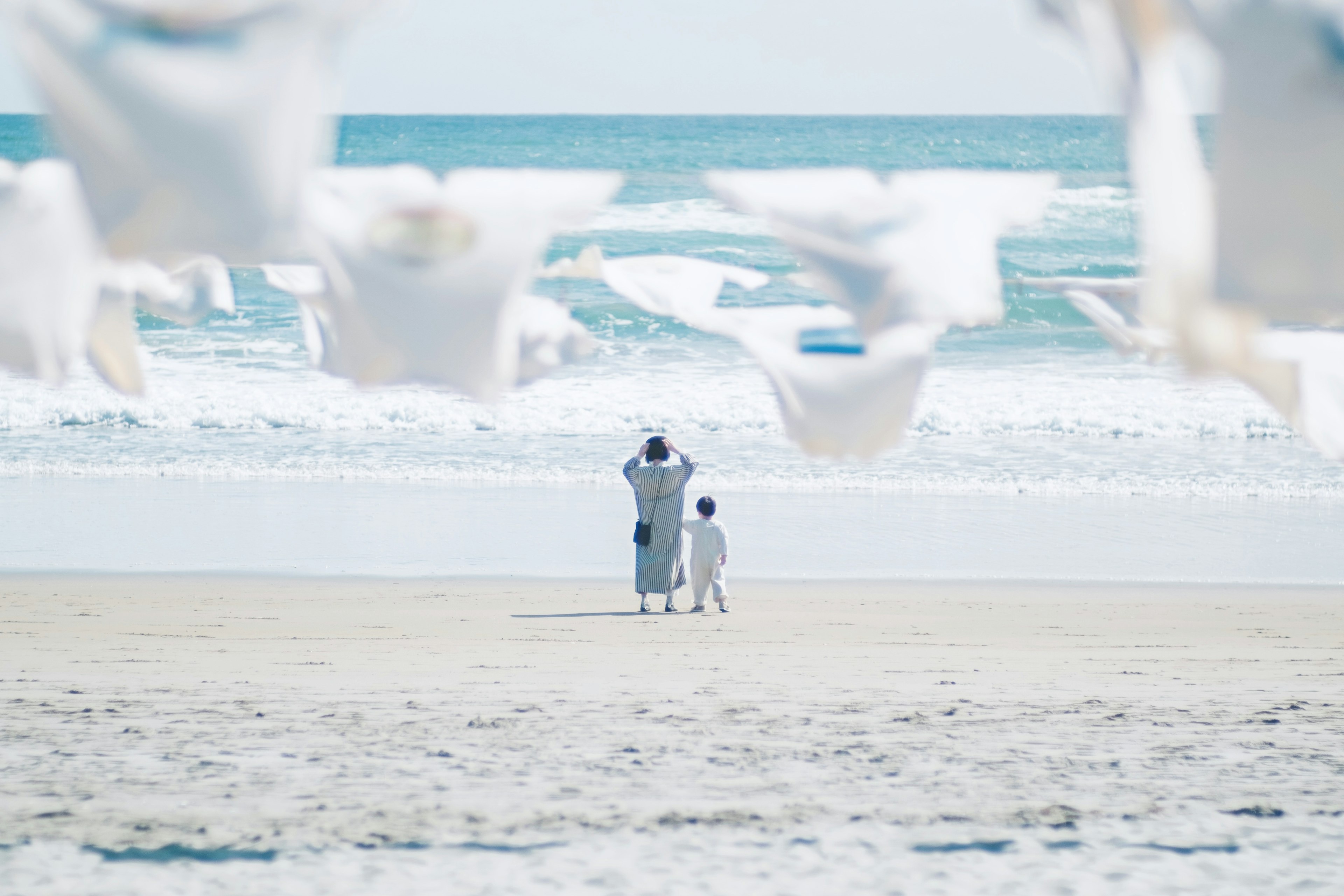 A parent and child standing by the beach with white fabric blowing in the wind