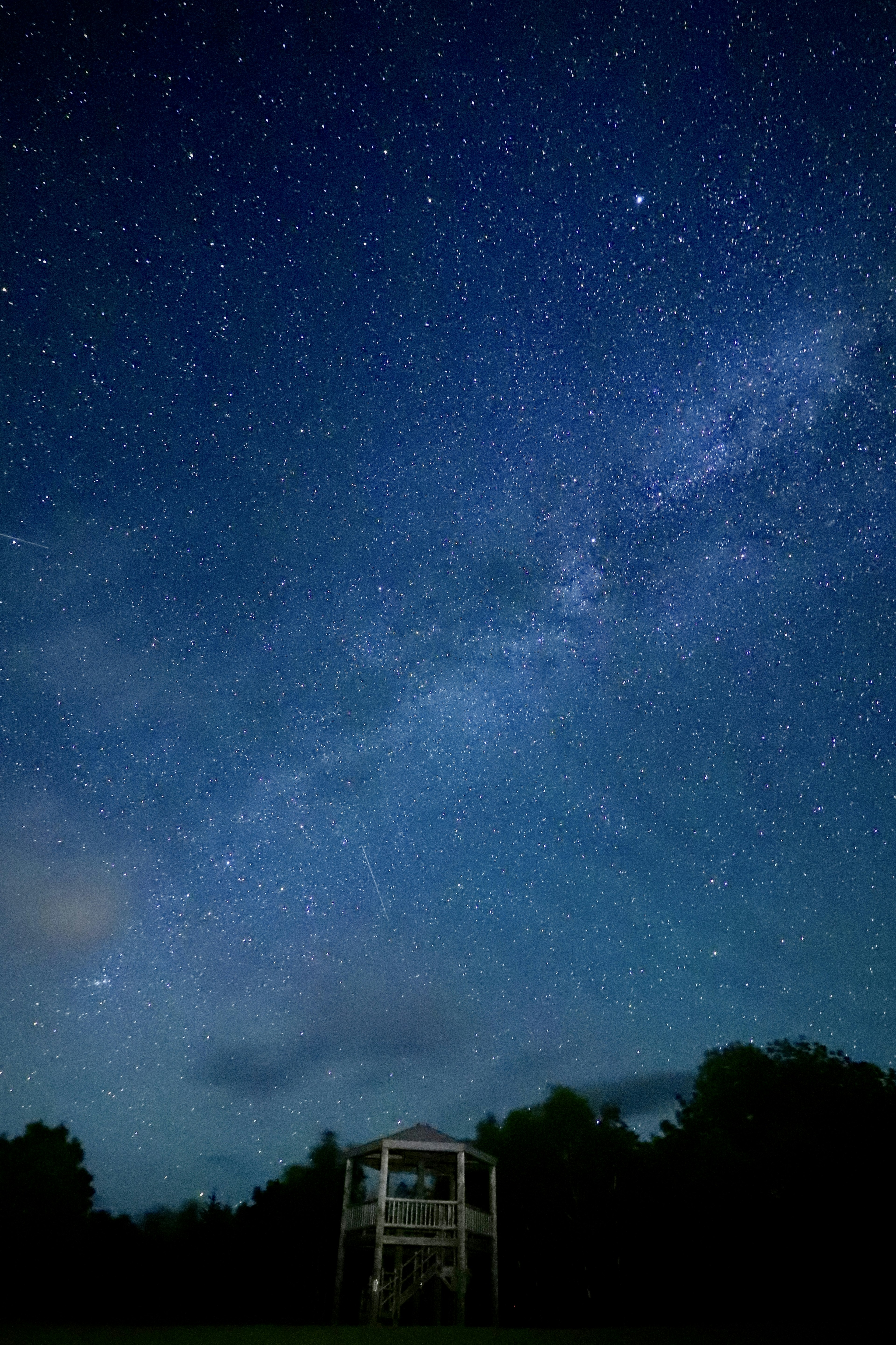 Night sky filled with stars and the Milky Way overlooking a small shelter