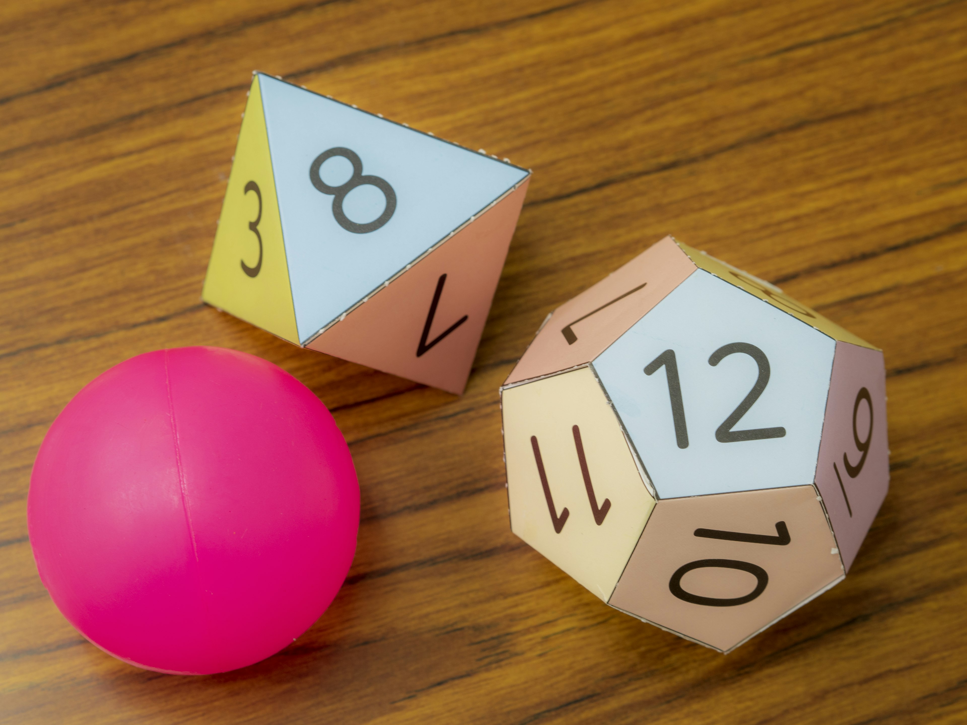 Une balle rose et des polyèdres numérotés sur une table en bois