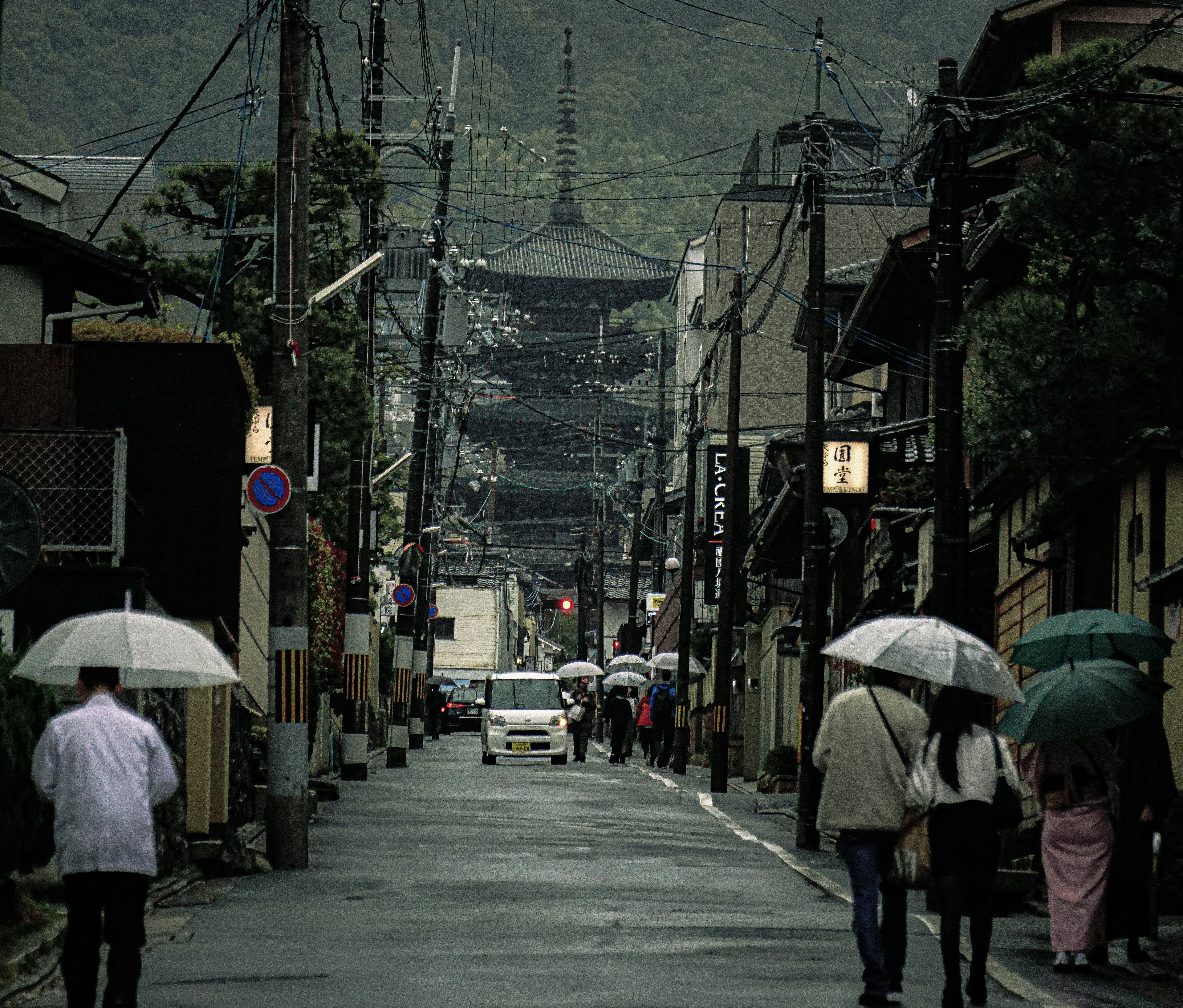 雨の中を歩く人々と古い建物が並ぶ通りの風景