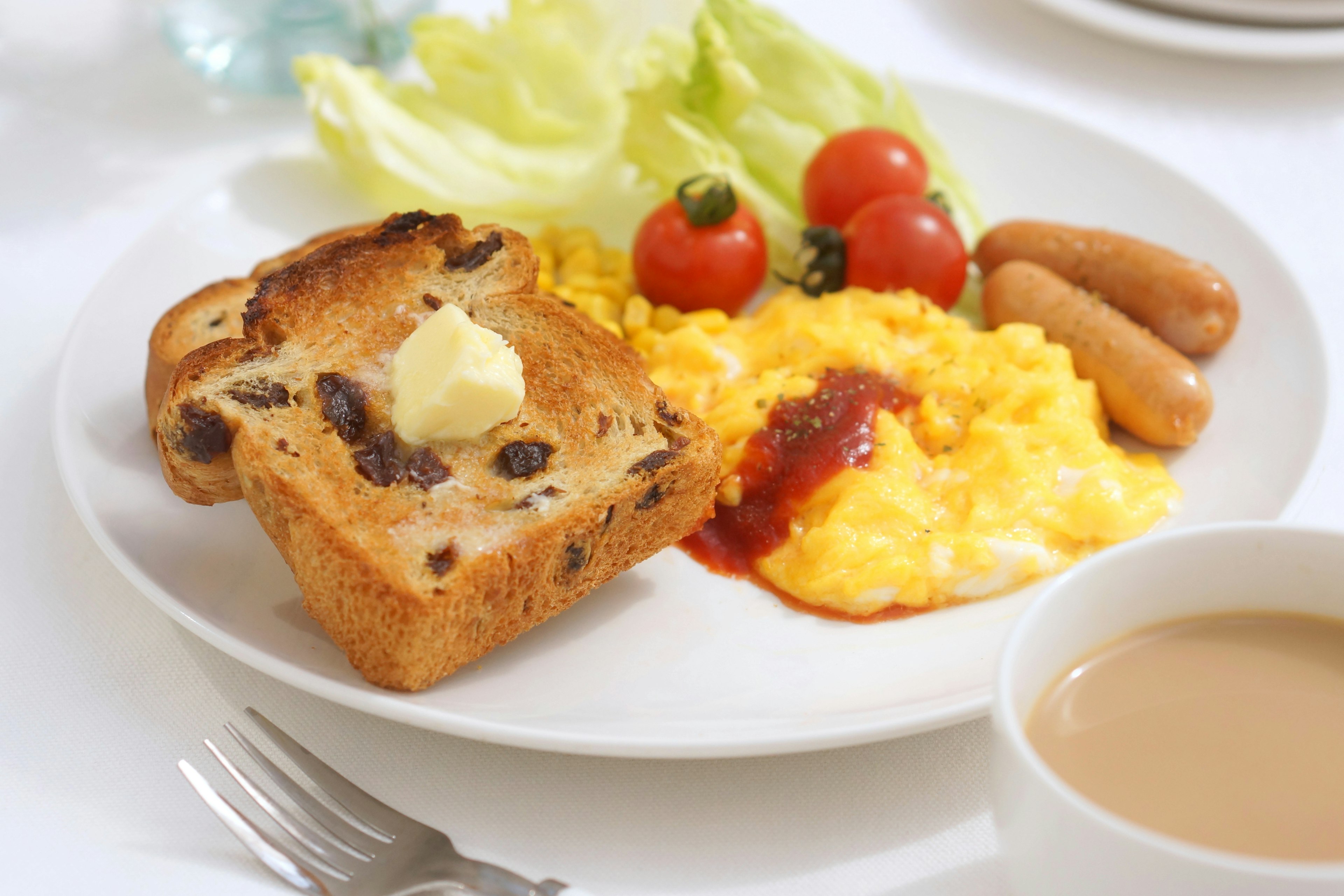 Breakfast plate featuring scrambled eggs, sausages, cherry tomatoes, lettuce, and buttered raisin bread