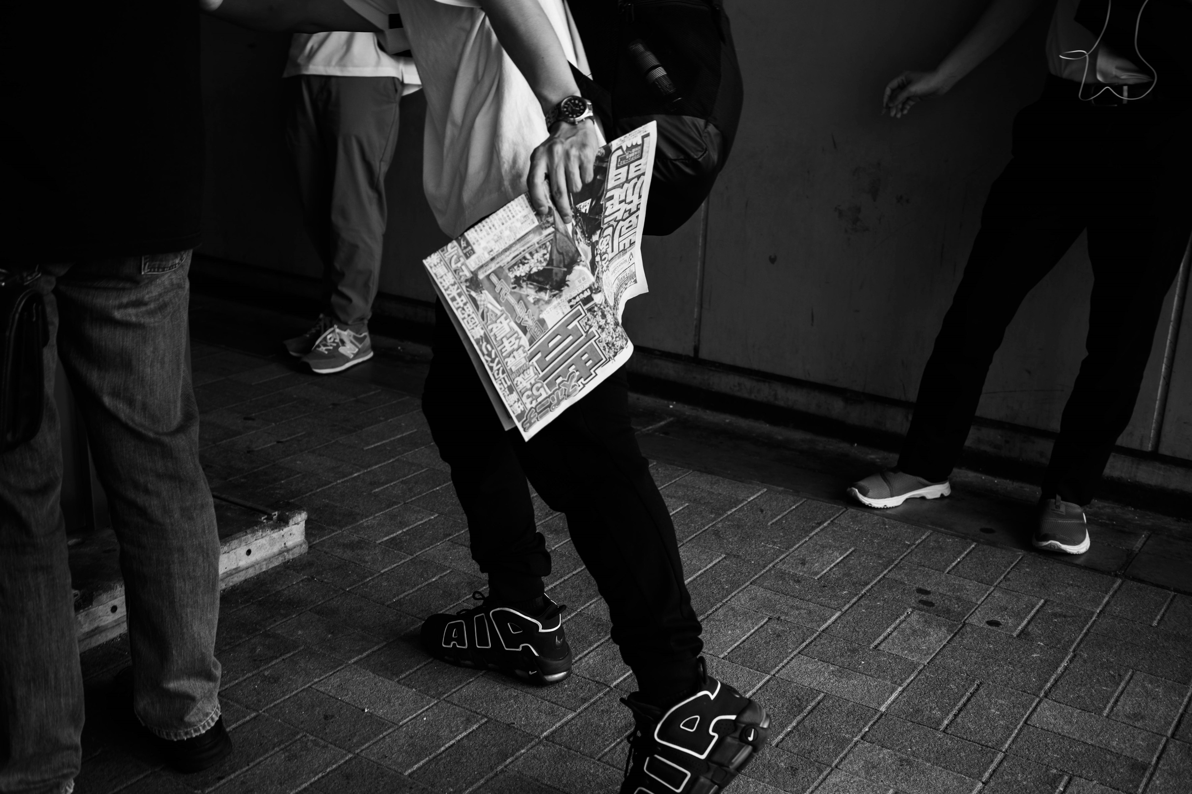 Photo en noir et blanc d'une personne tenant un journal entourée d'autres personnes