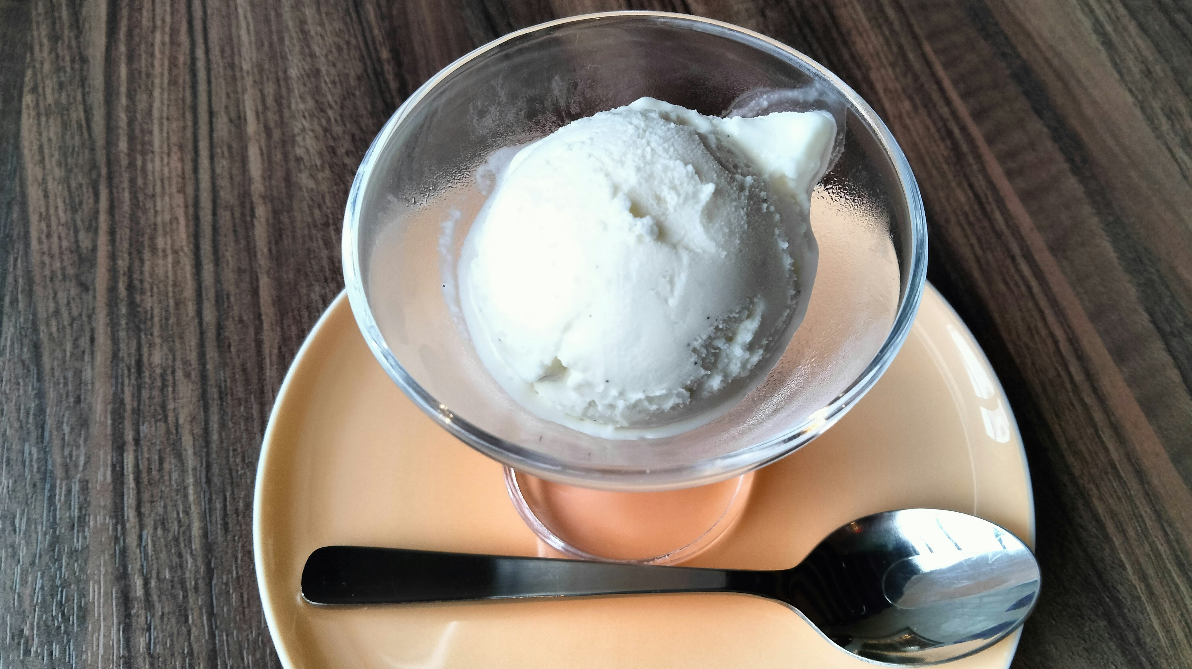 Scoop of white ice cream in a clear bowl served on a plate