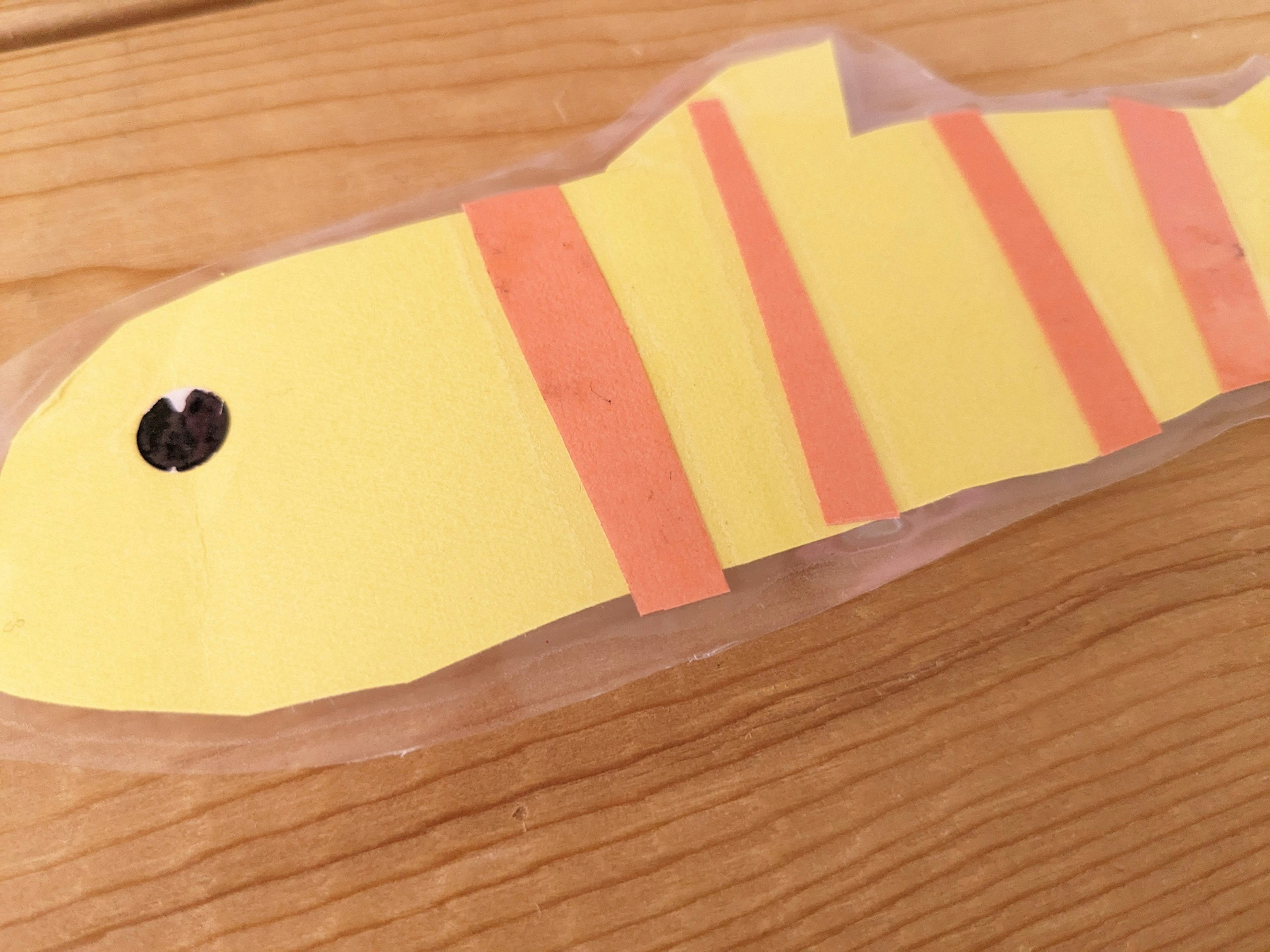 Crafted fish shape made from yellow paper with orange stripes and a black eye