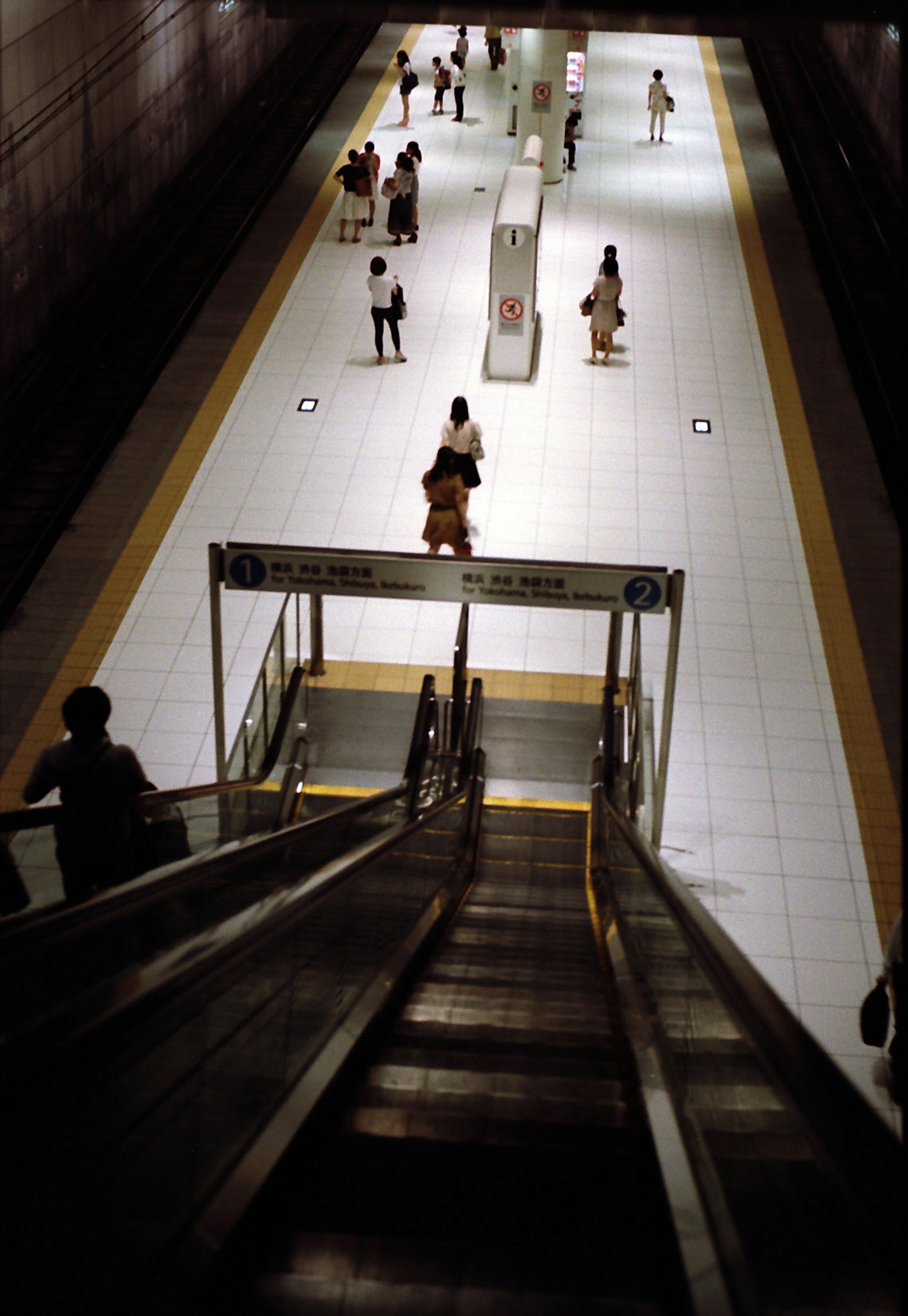 View from an escalator in a subway station people walking on a bright tiled walkway