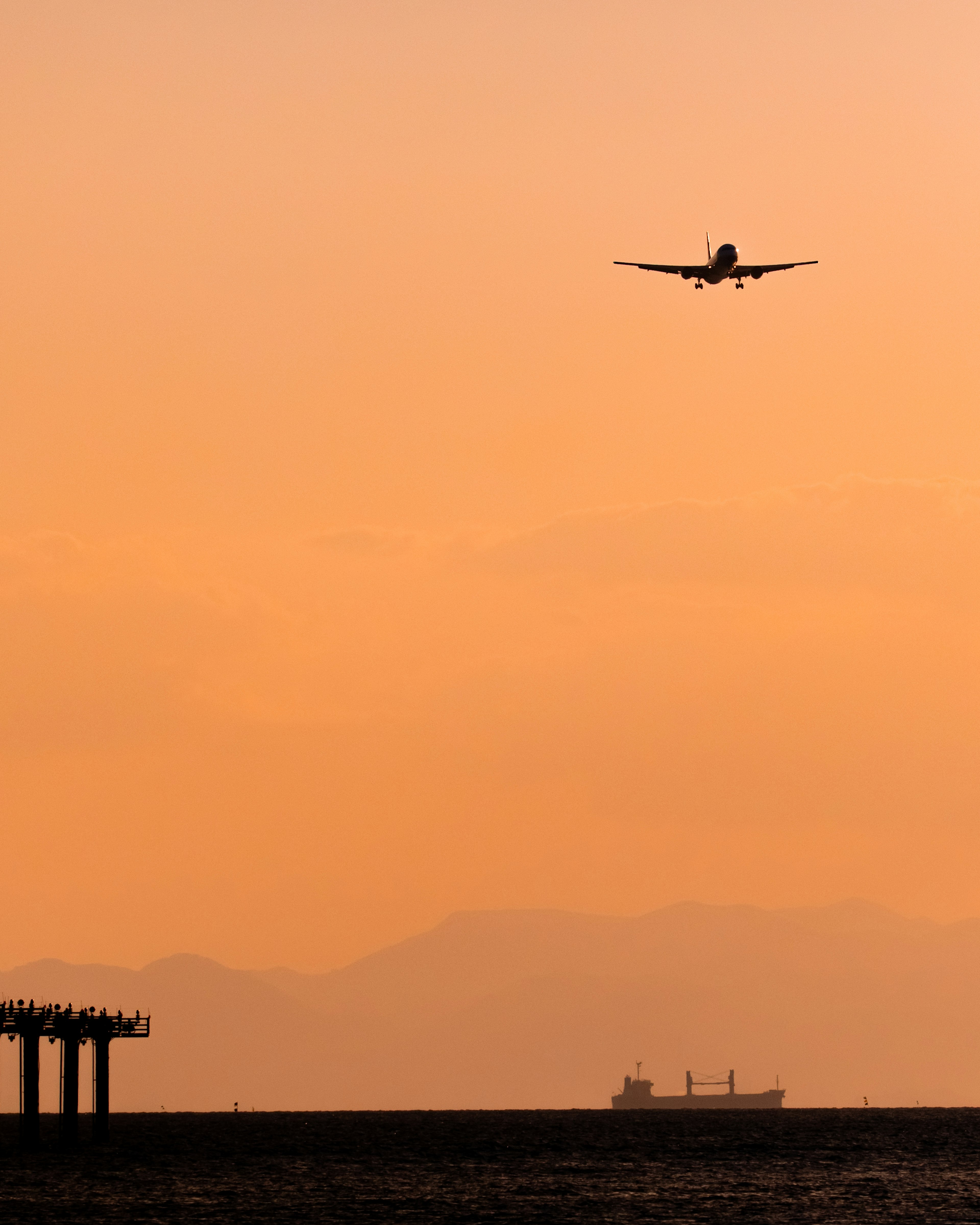 夕焼けの空に飛行機が飛び立つシルエットと海の景色