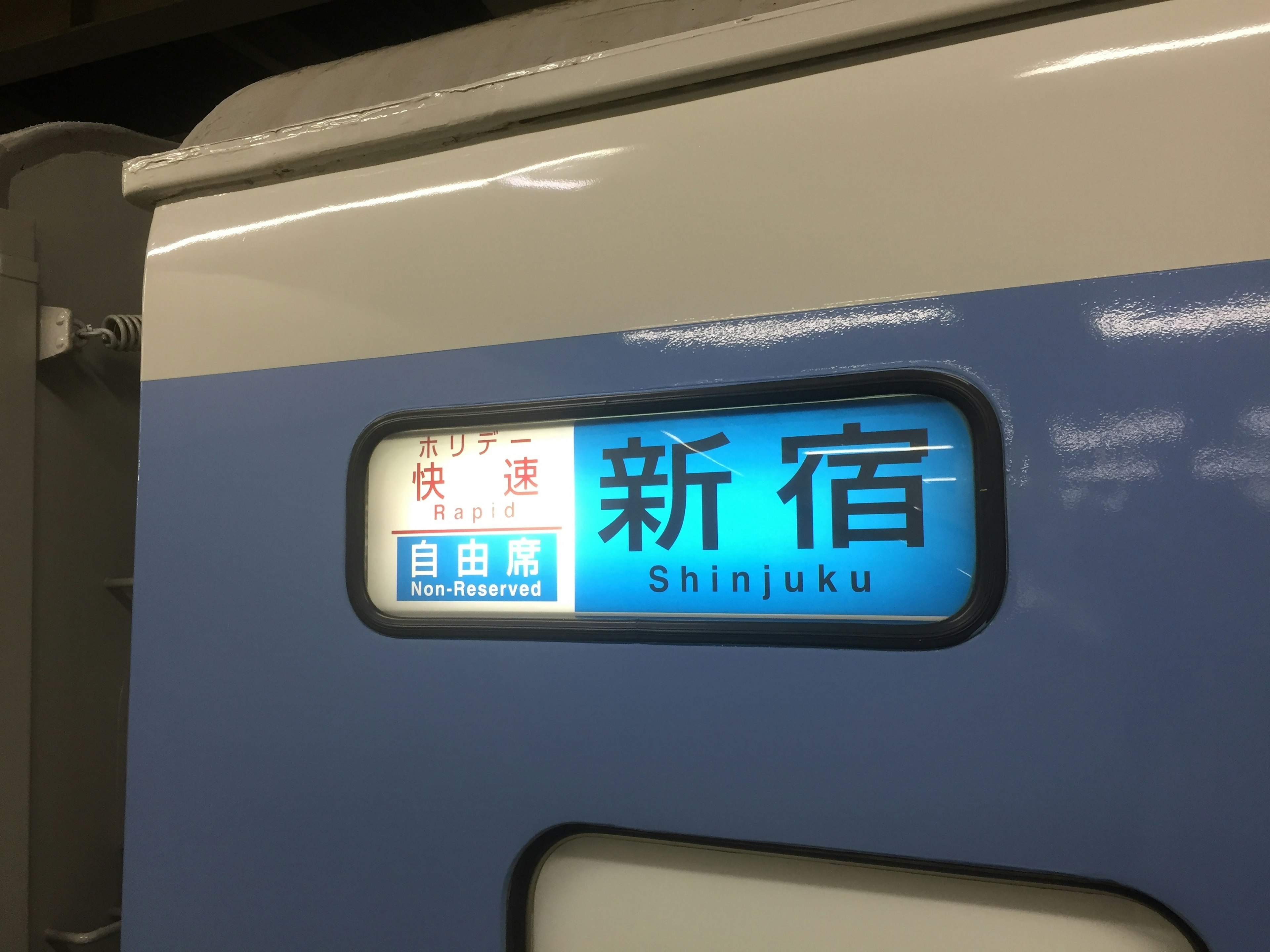 新宿行きの電車の表示が青い背景に白い文字で記載されている