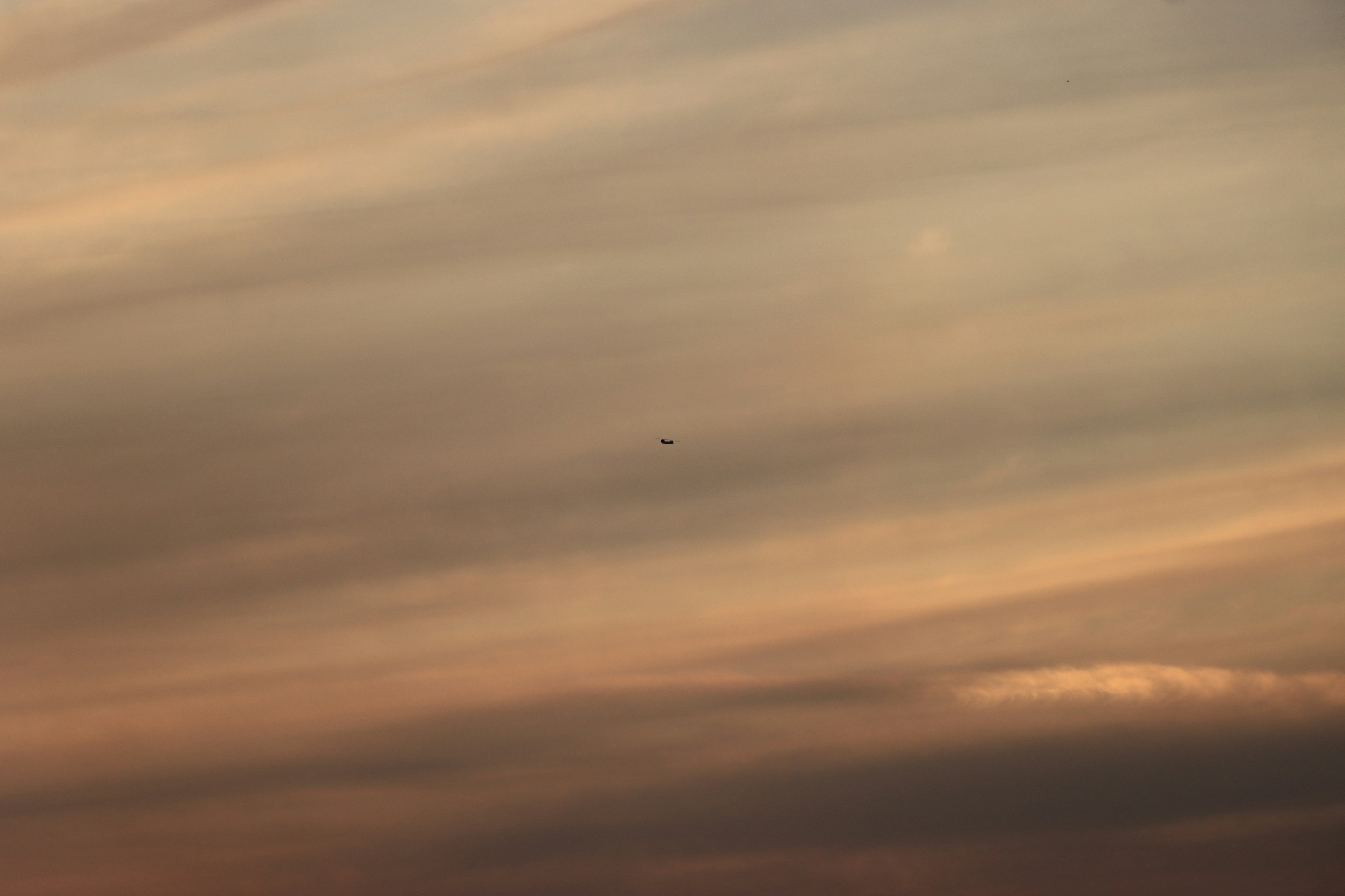 Un pequeño avión es visible en un cielo lleno de nubes suaves de color naranja y gris