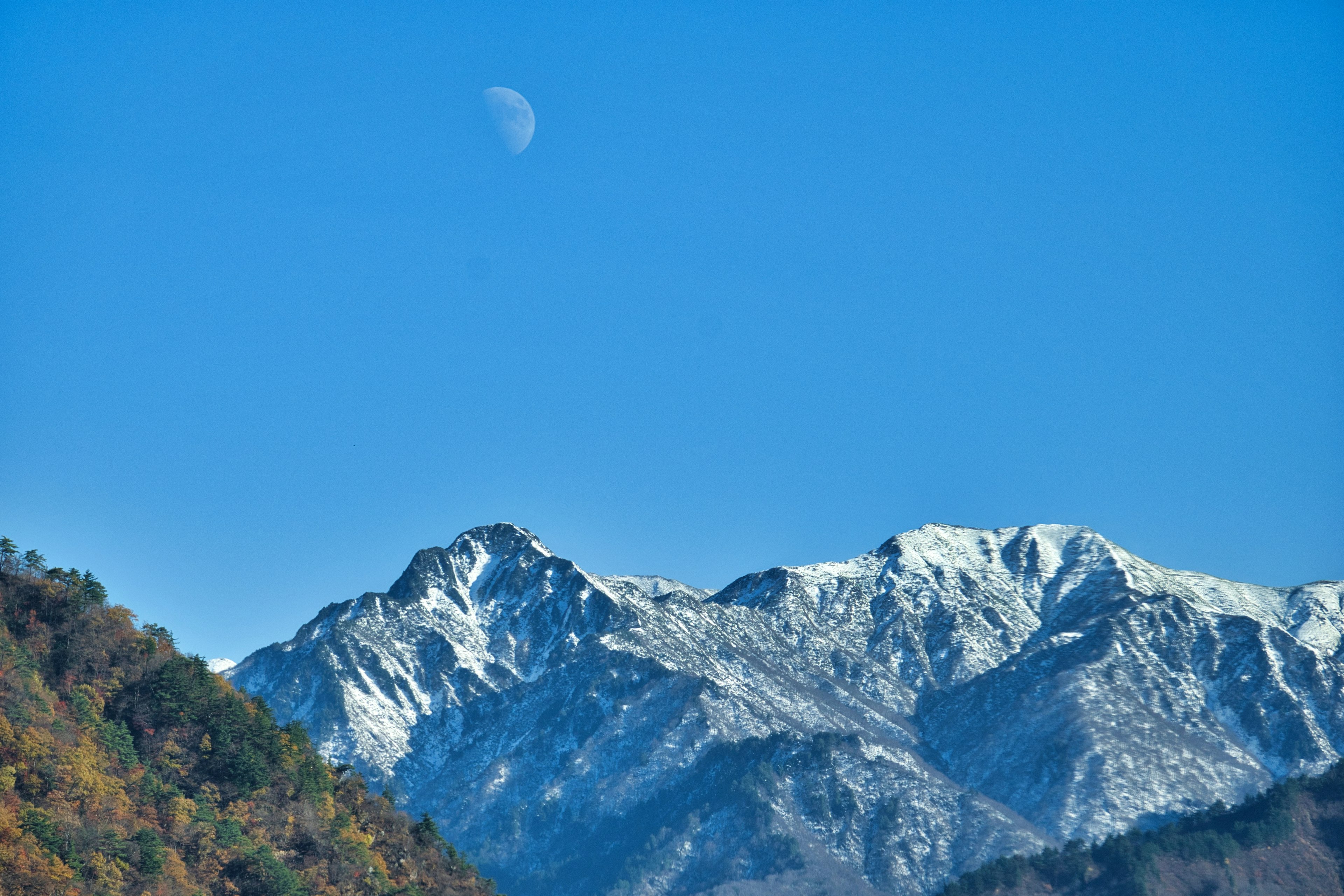 Malersicher Blick auf schneebedeckte Berge unter einem blauen Himmel mit sichtbarem Mond