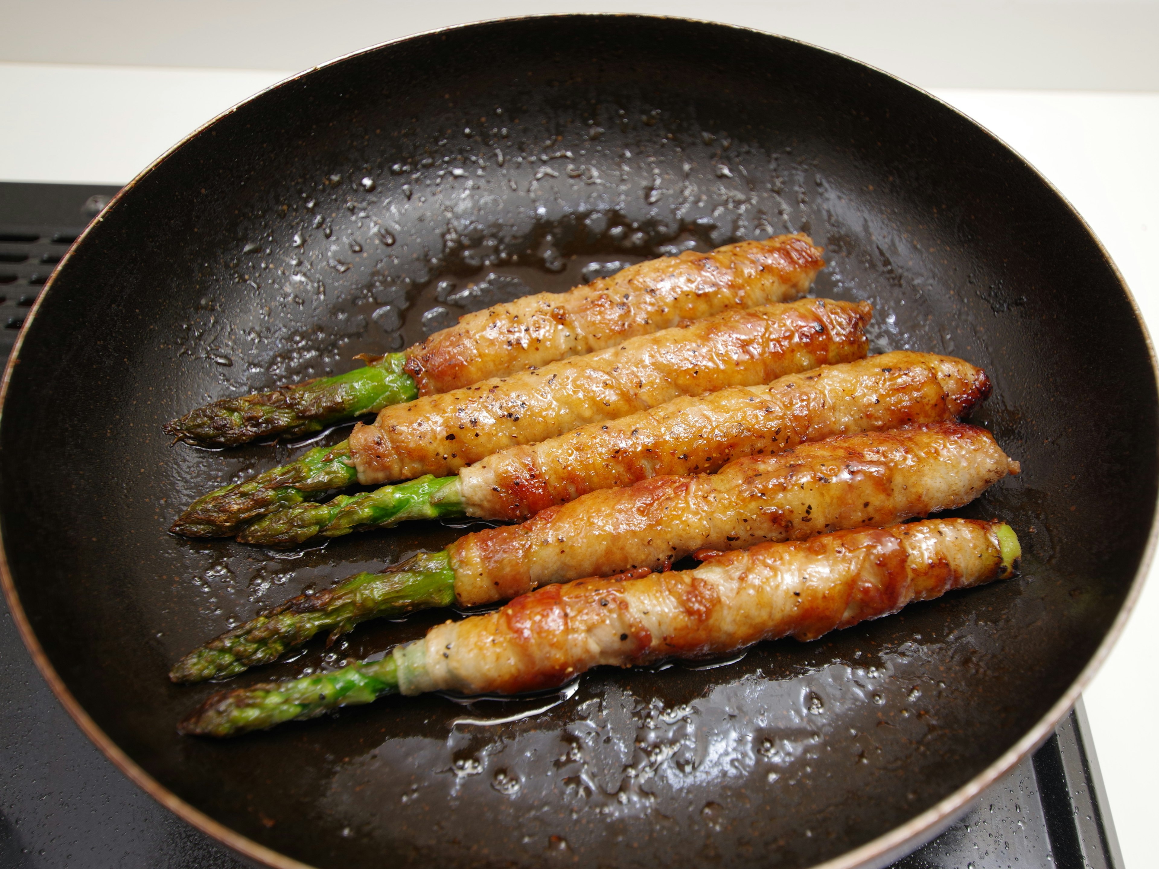 Ein Bund Spargel, eingewickelt in Speck, der in einer Pfanne brät