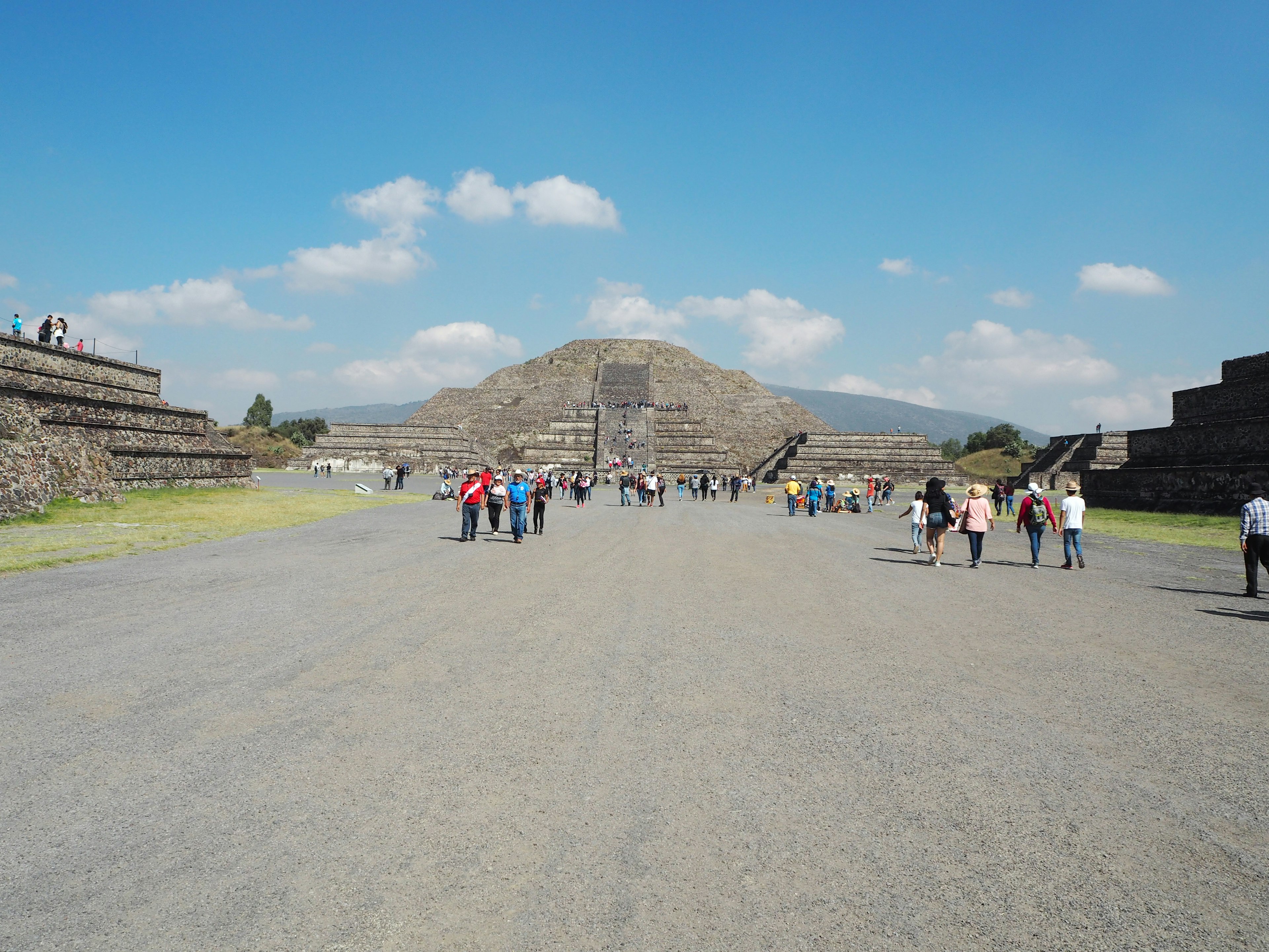 Tourists walking along a wide path with the Pyramid of the Sun in Teotihuacan