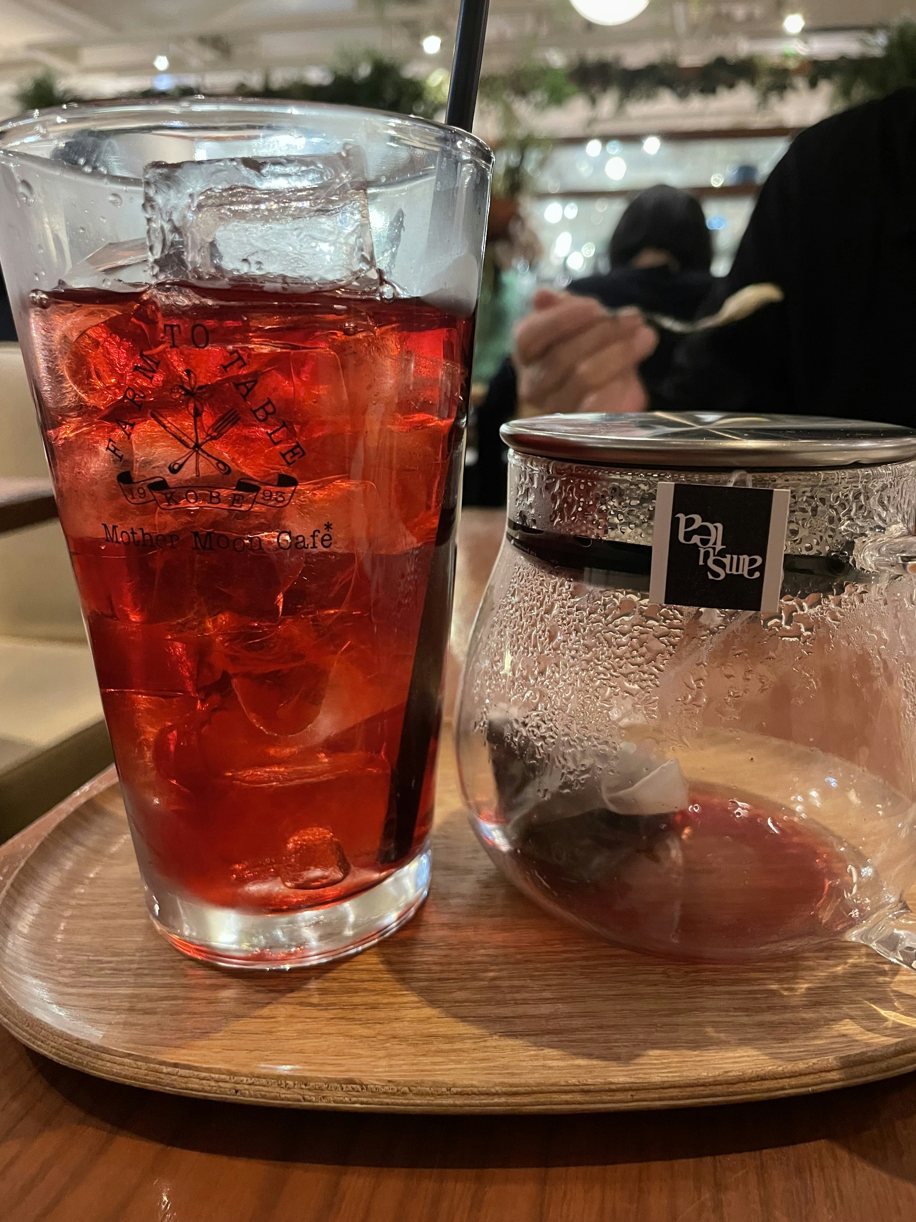 Un vaso de bebida roja con hielo en una bandeja de madera al lado de un pequeño frasco