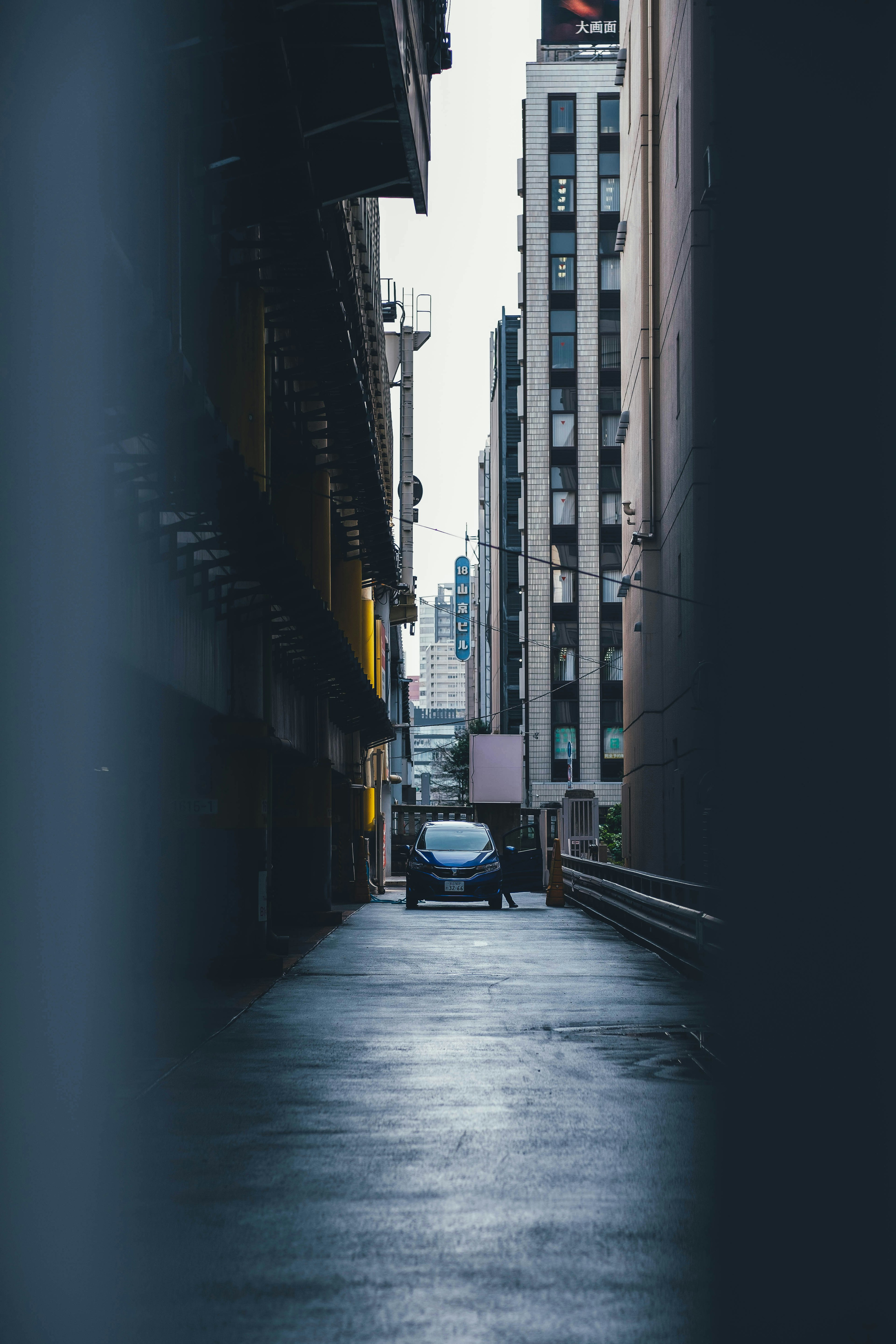 Narrow alleyway with a parked car and towering buildings