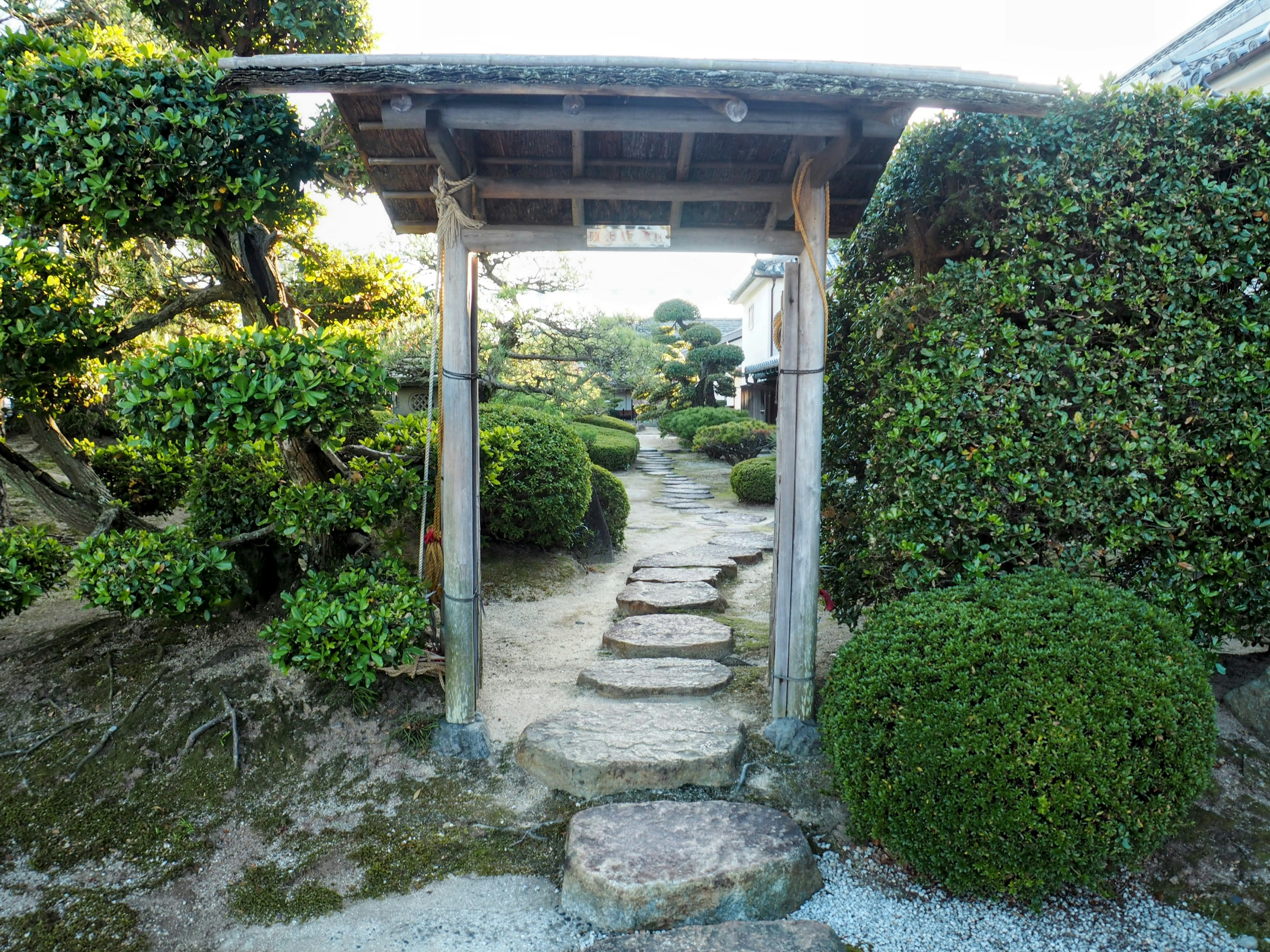 Entrada a un jardín japonés sereno con arbustos verdes y un camino de piedras