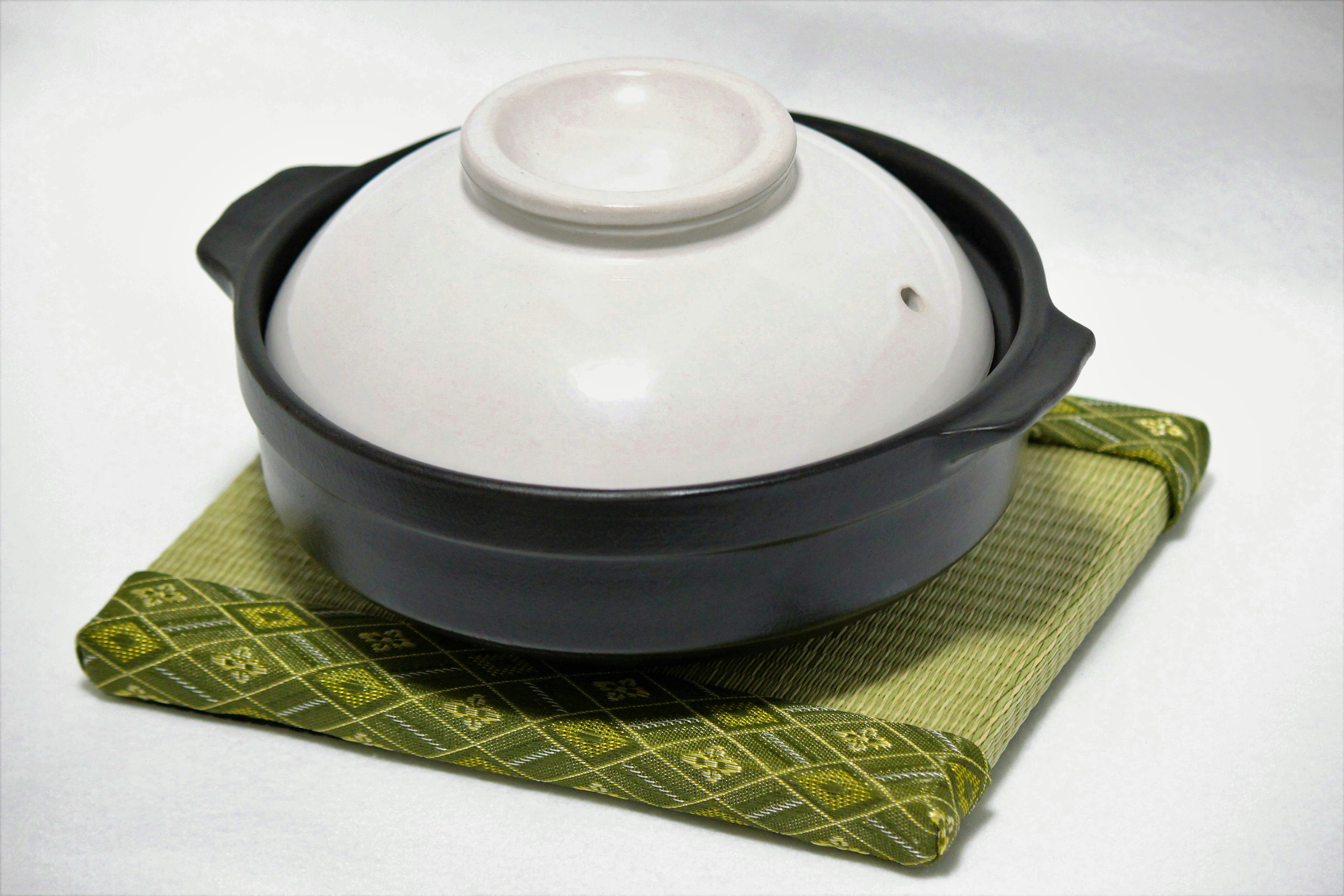 A cooking pot with a white lid set on a green mat